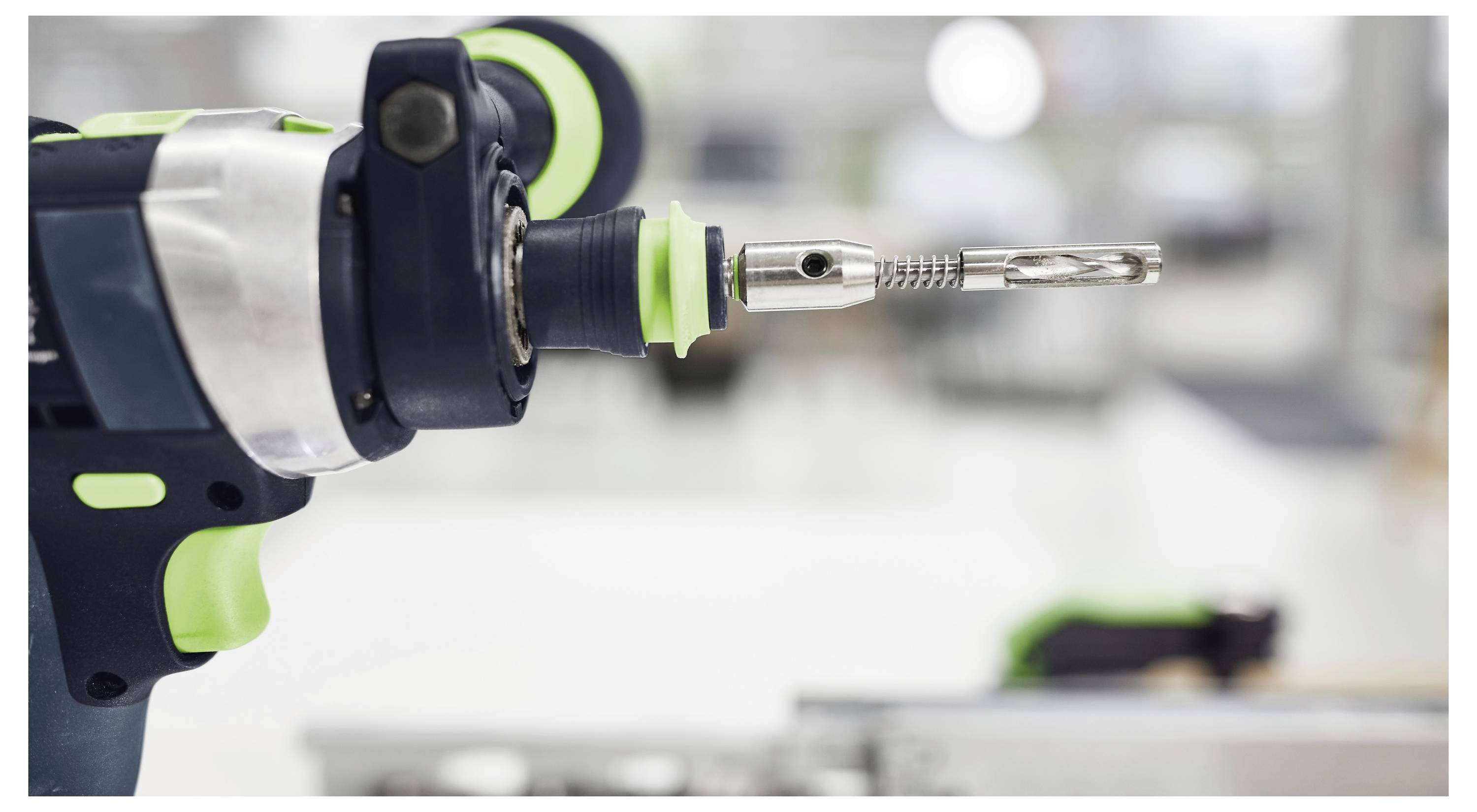 Eine Nahaufnahme einer Elektrobohrmaschine mit angespanntem Metallaufsatz, eingebettet in eine Werkstattumgebung. Die Bohrmaschine verfügt über grüne Akzente.