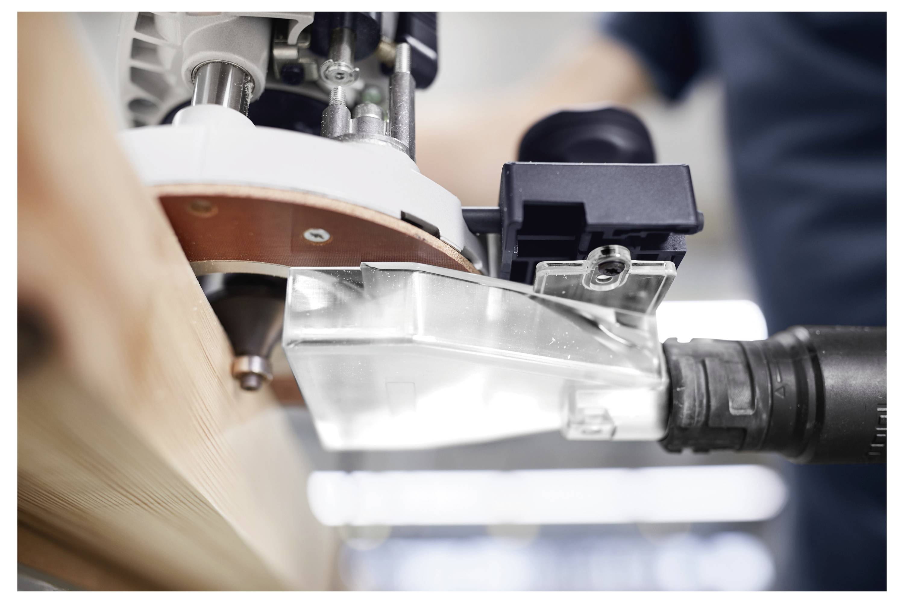 Ein Mann mit Schutzbrille bedient ein Elektrowerkzeug auf einem Holzbrett in einer Holzwerkstatt, mit Holzregalen im Hintergrund.