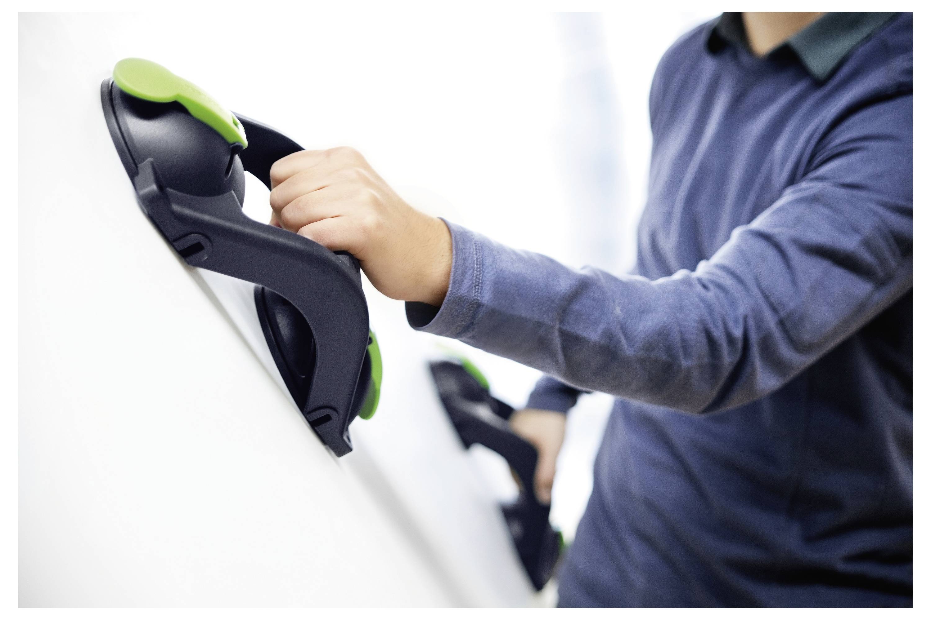 Person, die ergonomische Saugnapfheber verwendet, um eine große, glatte Oberfläche anzuheben, was auf eine Aufgabe hinweist, die mit der Bewegung oder Installation schwerer Platten verbunden ist.