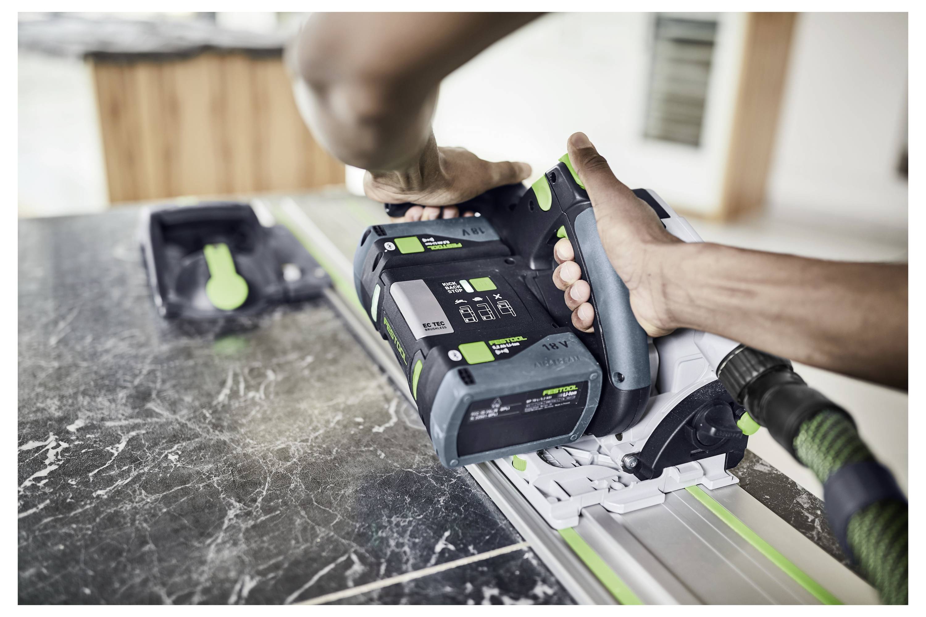Eine Person bedient mit ihren Händen ein Elektrowerkzeug auf einer Schiene, um Stein zu schneiden. Die Ausrüstung ist modern und hat grüne Akzente.