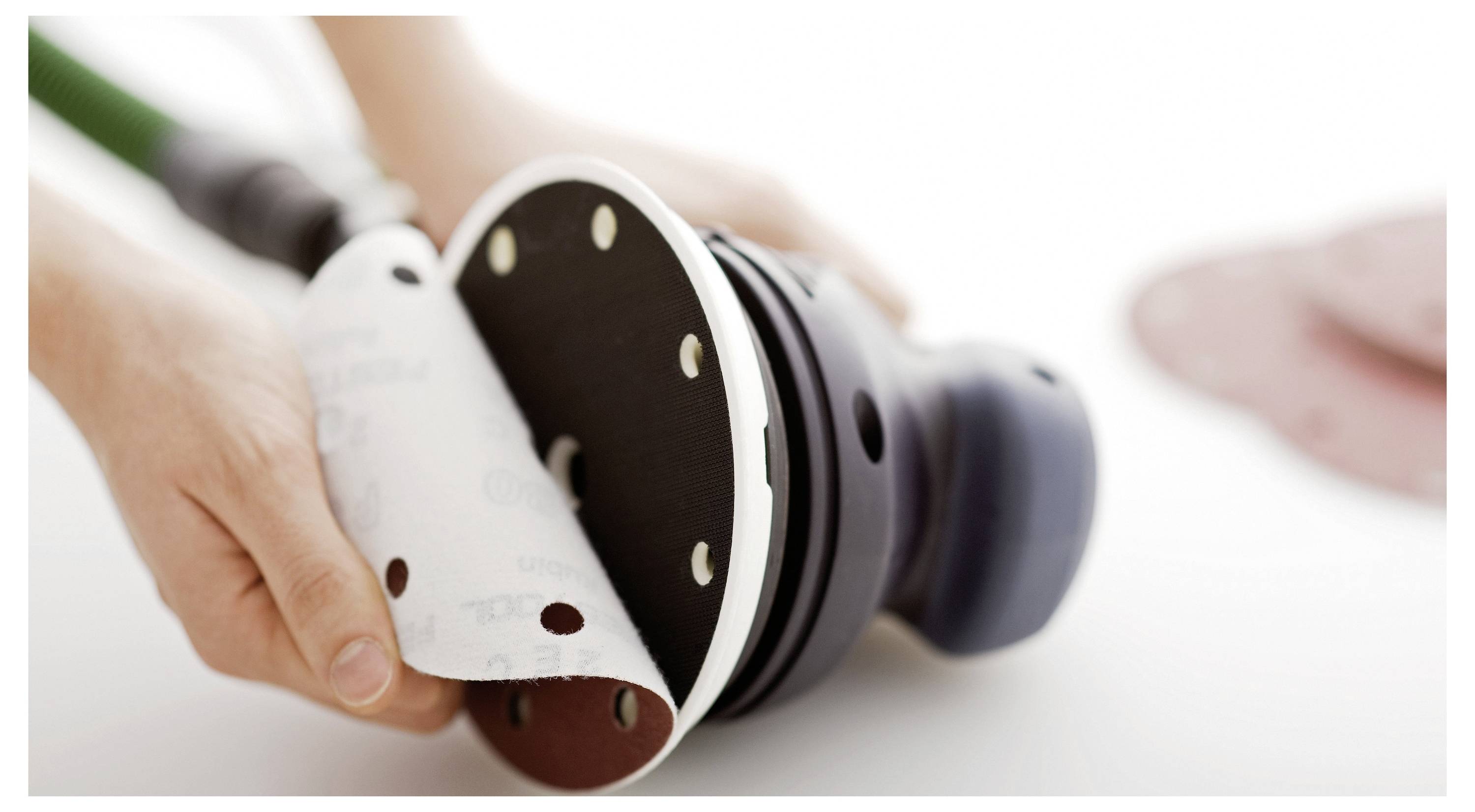 Eine Person bringt Schleifpapier auf einen tragbaren Elektroschleifen an und bereitet es zur Verwendung vor.