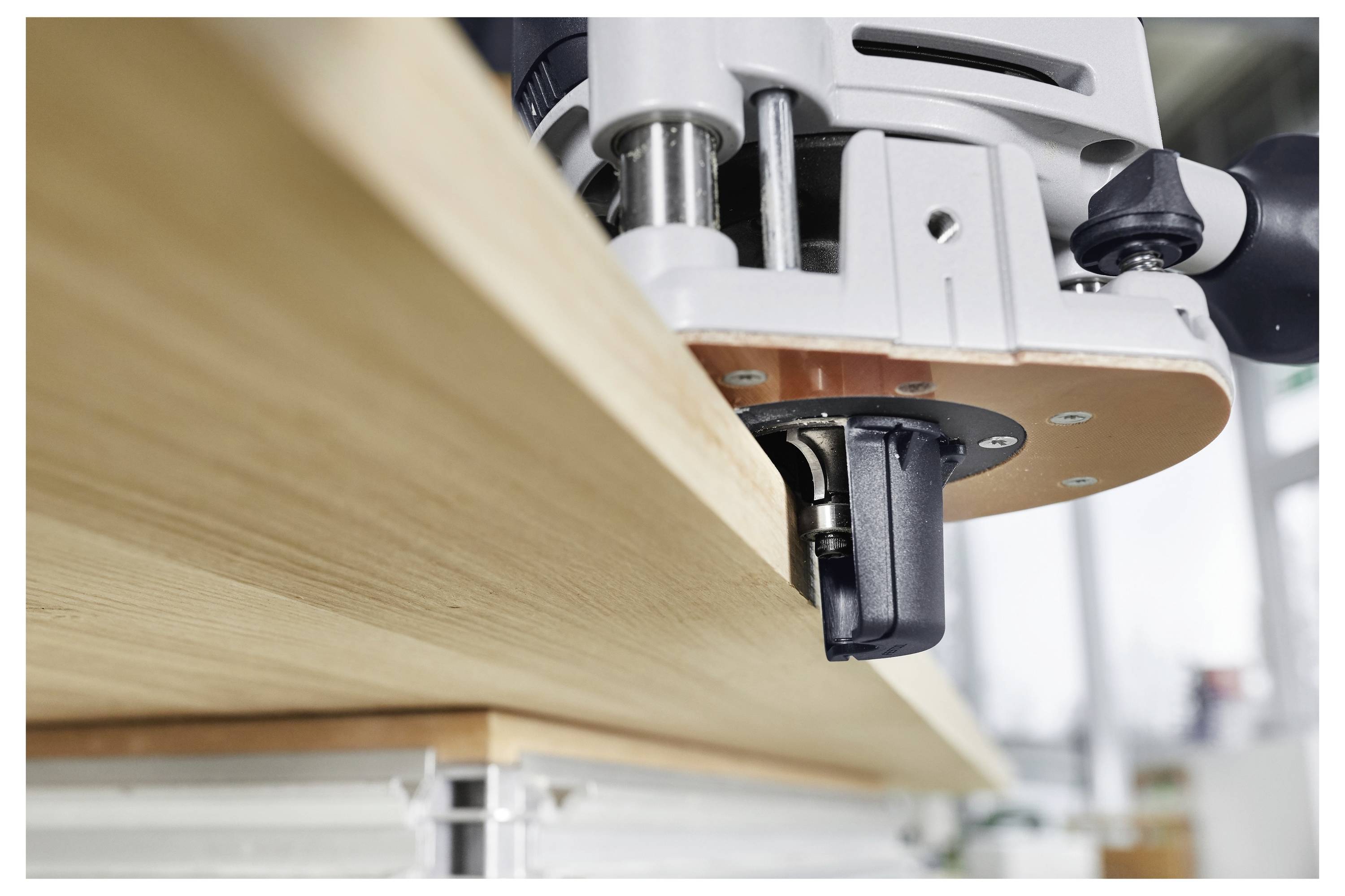 Nahaufnahme einer Holzfräsmaschine, die die Kante eines Holzbretts trimmt, mit glatter Oberfläche und präzisem Schnitt in einer Werkstattumgebung.