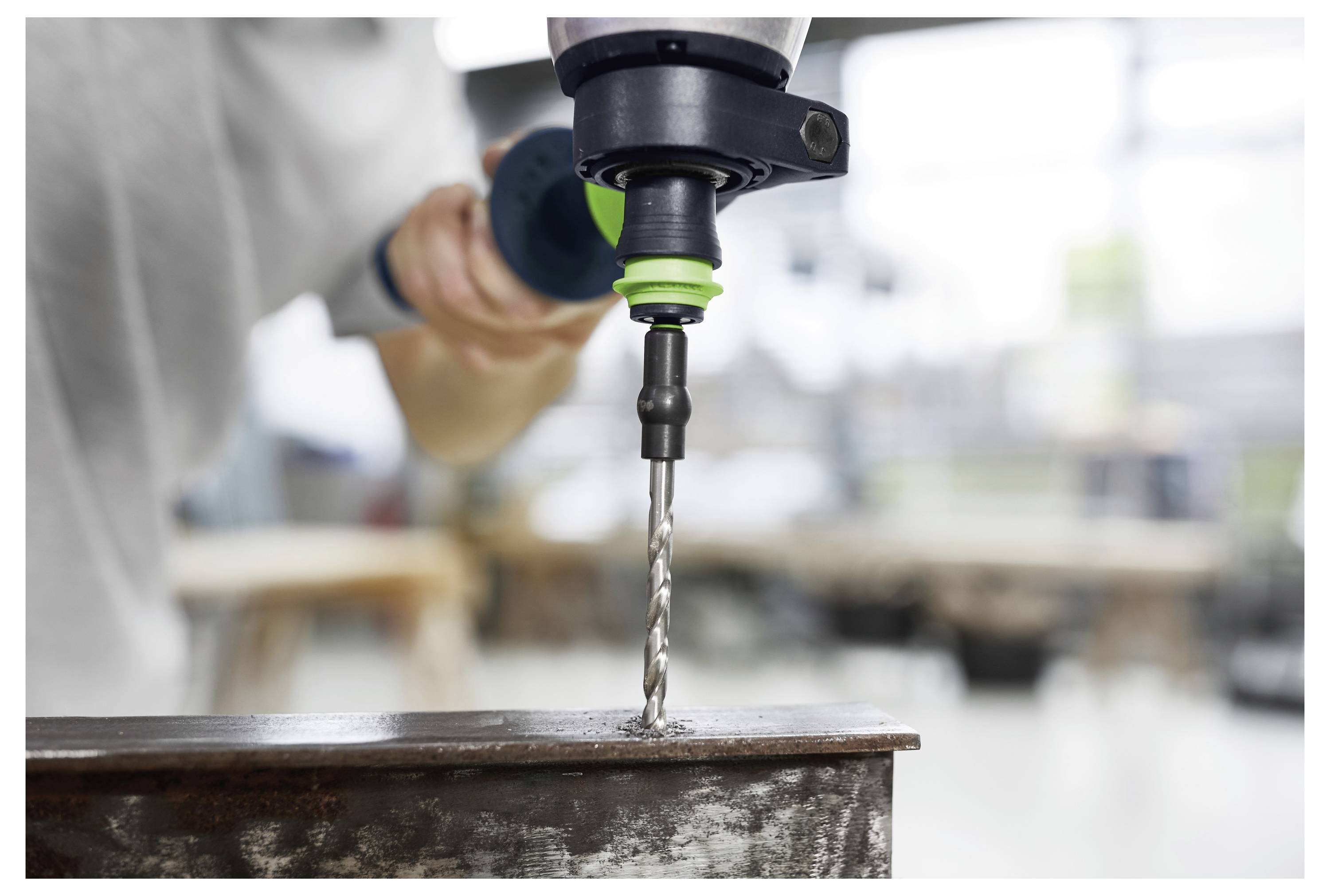 Eine Person nutzt eine Elektrobohrmaschine mit einem Metallbohrer, um ein Loch in einen Stahlträger in einer Werkstattatmosphäre zu bohren.