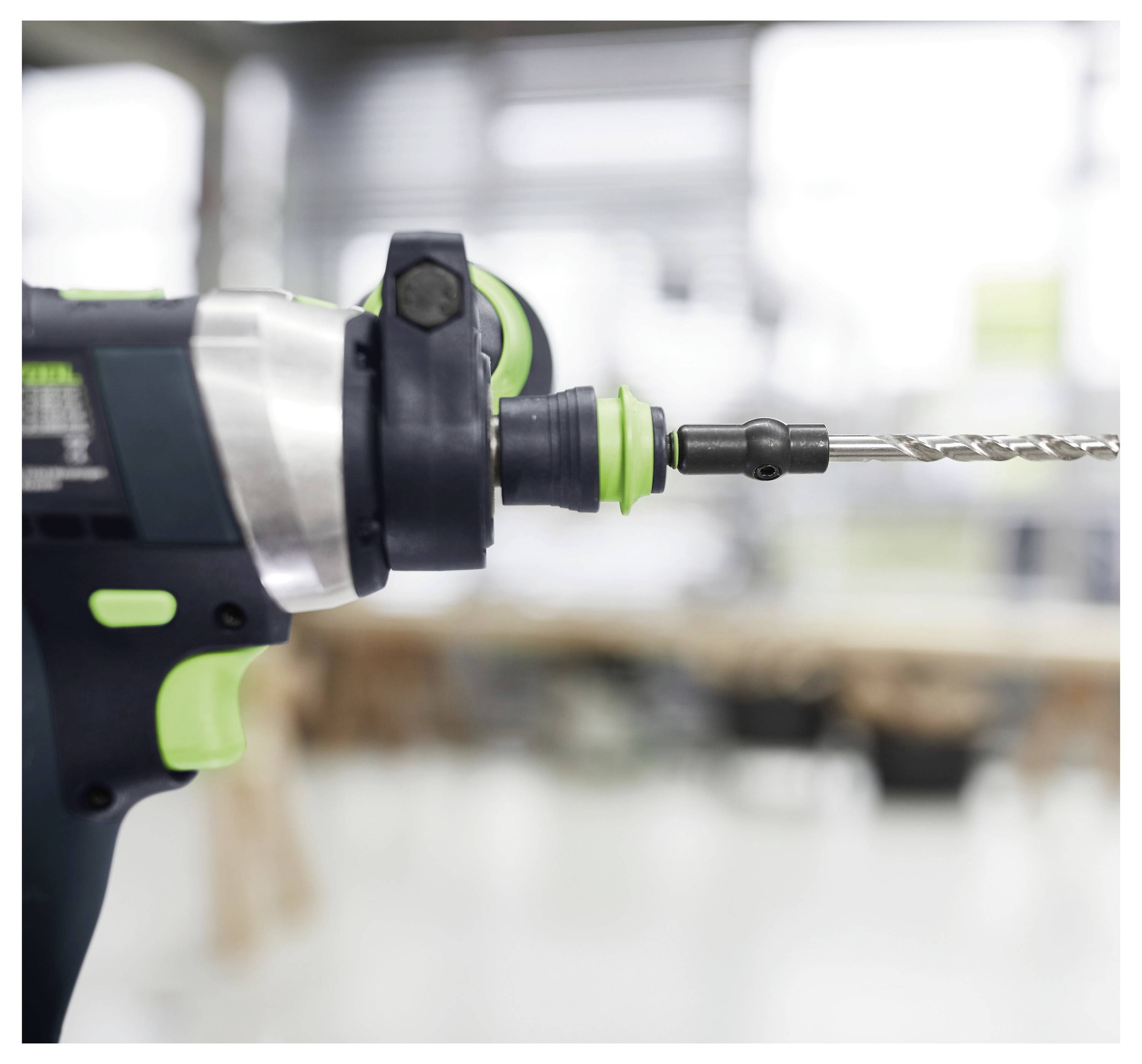 Eine Nahaufnahme einer elektrischen Bohrmaschine mit sichtbarem Bohraufsatz vor einem unscharfen Werkstatt-Hintergrund, was eine Arbeitsumgebung andeutet.