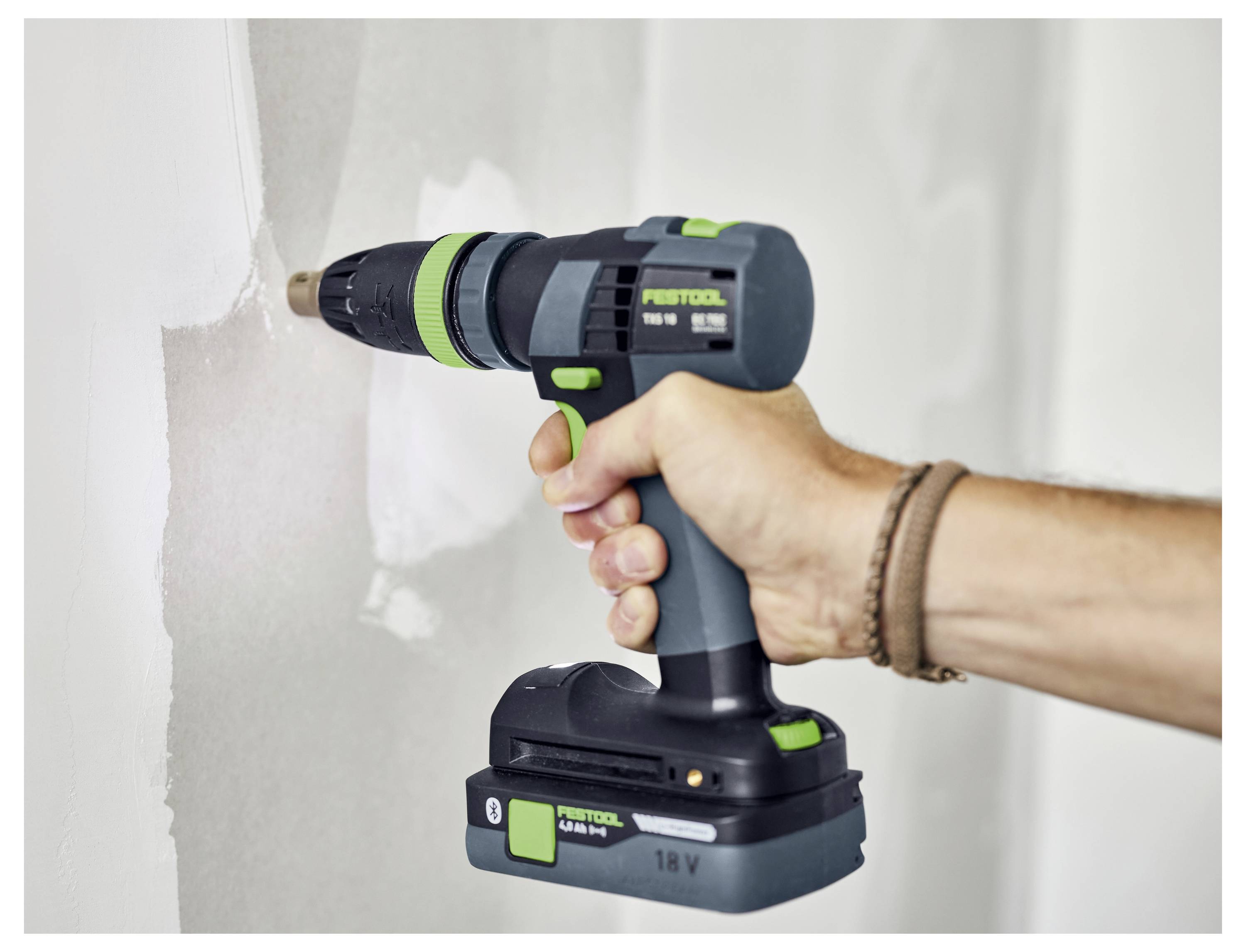 Eine Person, die einen kabellosen Bohrschrauber verwendet, um eine Schraube in eine Wand zu treiben, wobei die Griffigkeit und das Design des Werkzeugs mit sichtbarer Markenbezeichnung hervorgehoben werden.