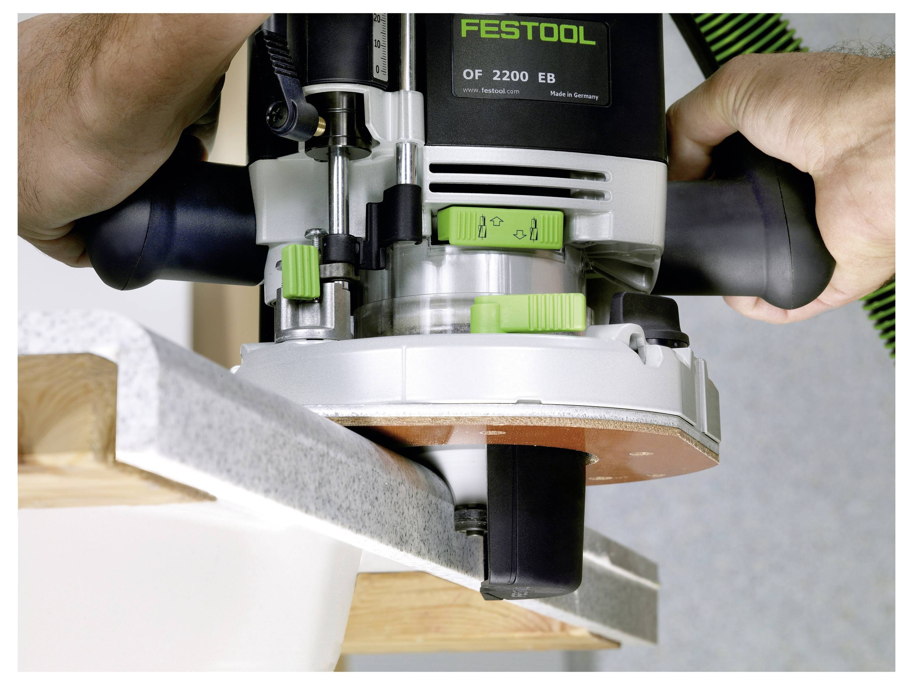 Eine Person benutzt ein Elektrowerkzeug mit grünen Einstellungen, um Holz zu schneiden oder zu bearbeiten, und zeigt eine Nahaufnahme der Werkzeugeinwirkung auf eine Arbeitsplattenkante.
