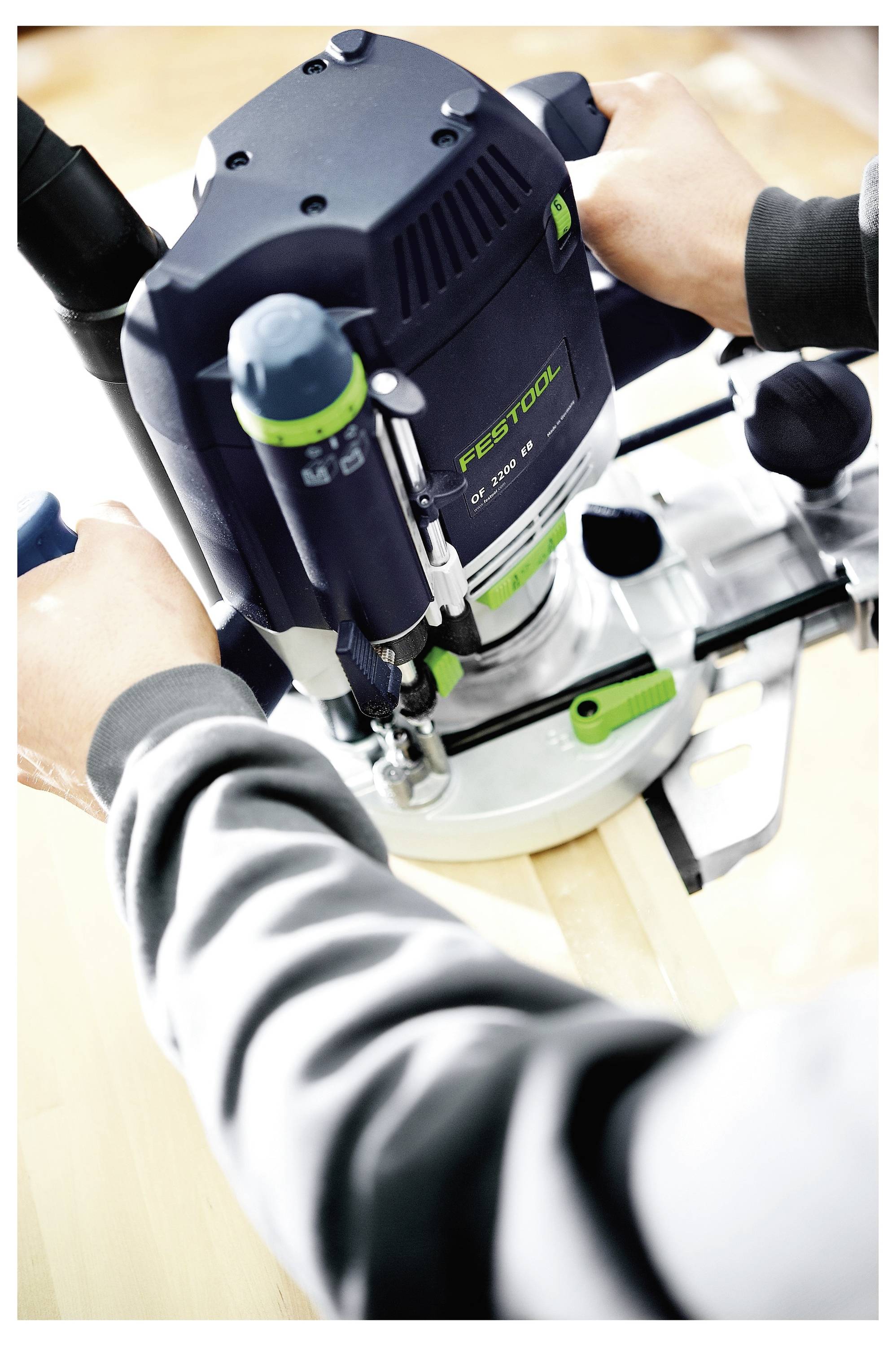 Eine Person nutzt einen Festool-Fräser auf einer Holzoberfläche und stellt die Einstellungen für Präzision ein. Die Hände greifen das Werkzeug und gewährleisten eine genaue Bedienung.