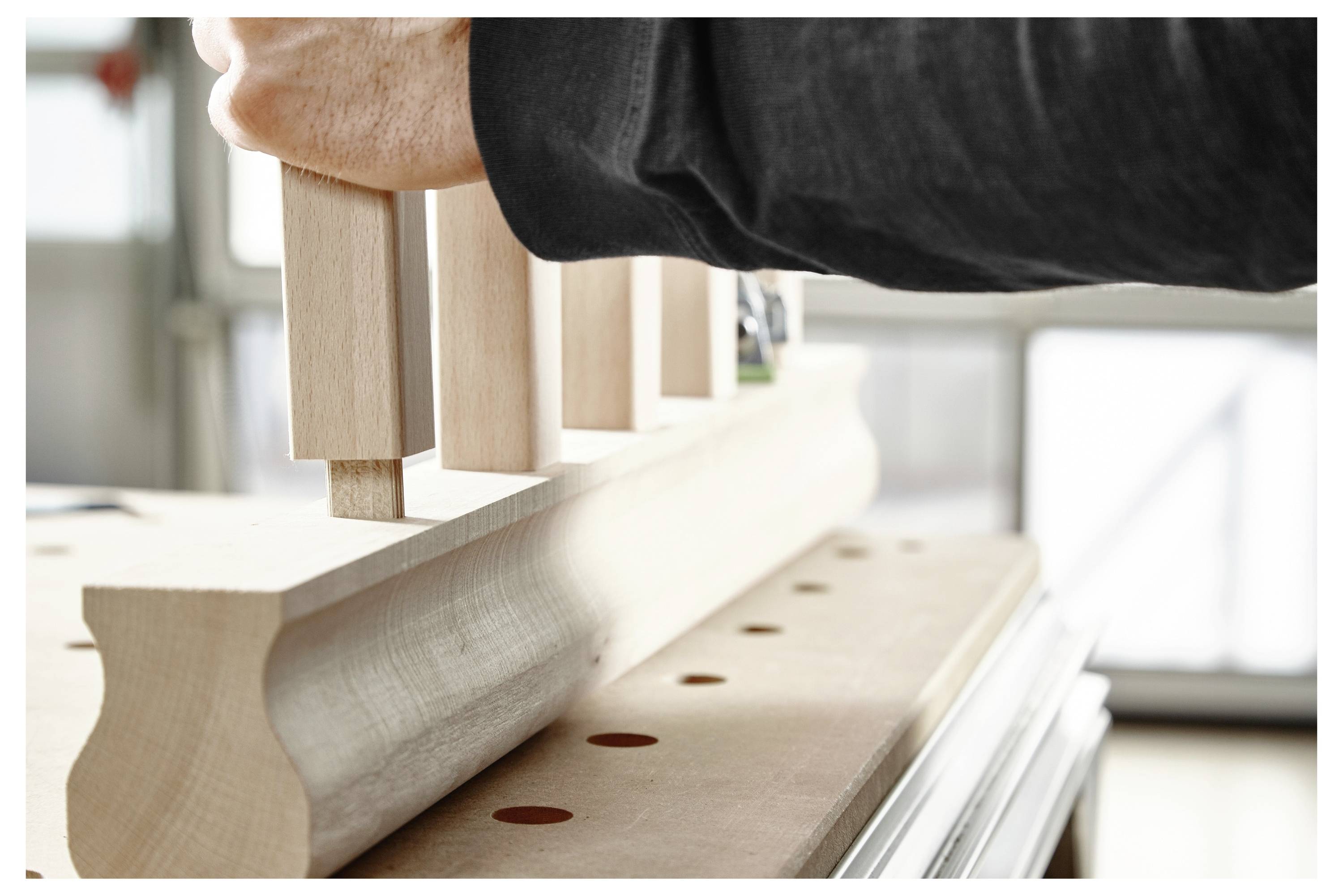 Eine Person fügt hölzerne Zapfen- und Nuten-Verbindungen über einer Werkbank zusammen und demonstriert präzise Holzbearbeitung in einer gut beleuchteten Werkstatt.