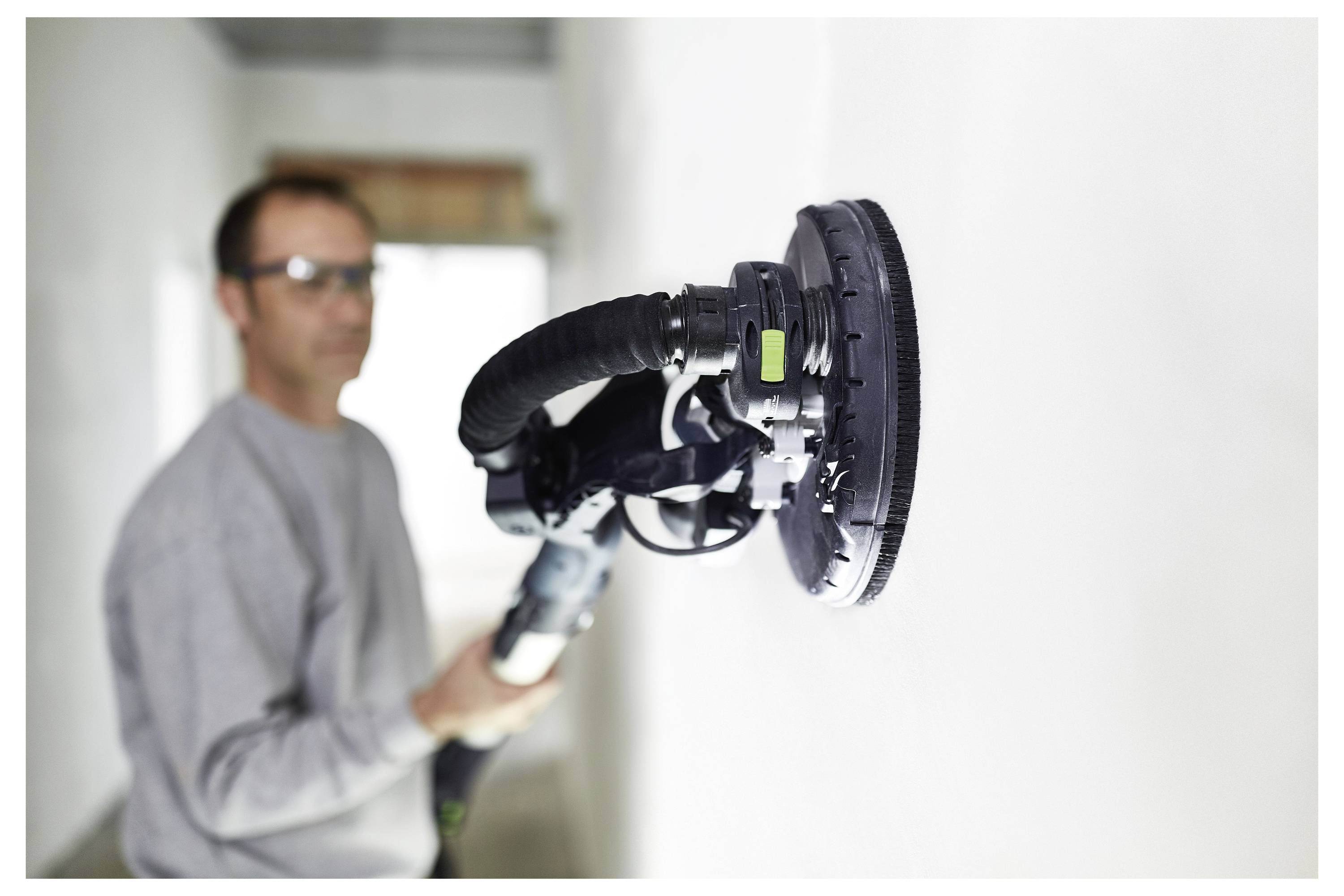 Eine Person glättet eine Wand mit einem tragbaren elektischen Schleifeif in einem Raum und konzentriert sich dabei auf das Finish der Oberfläche zum Anstreichen oder Dekorieren.