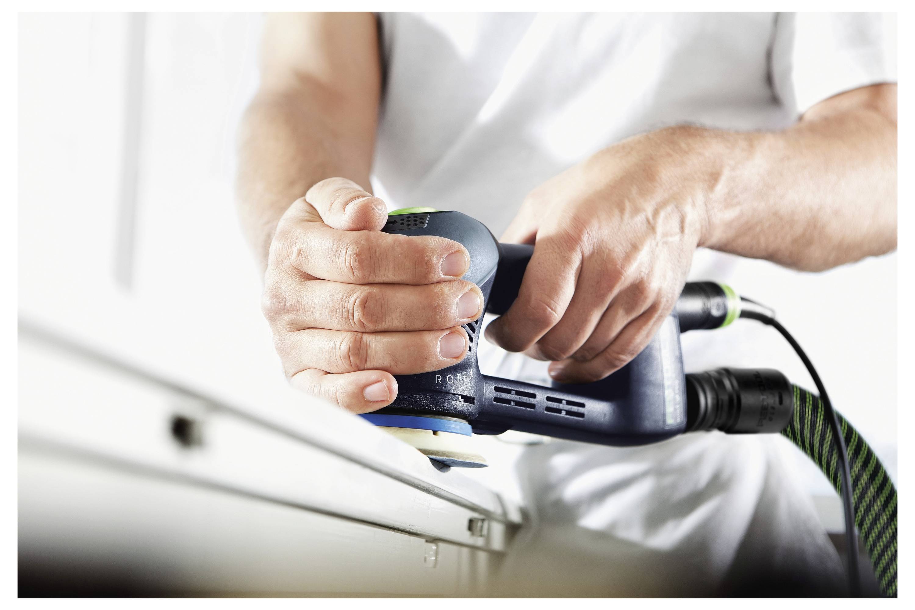 Nahaufnahme von Händen, die einen Elektroschlifer auf einer Holzoberfläche bedienen, wobei die Kanten mit präzisen Bewegungen geglättet werden.