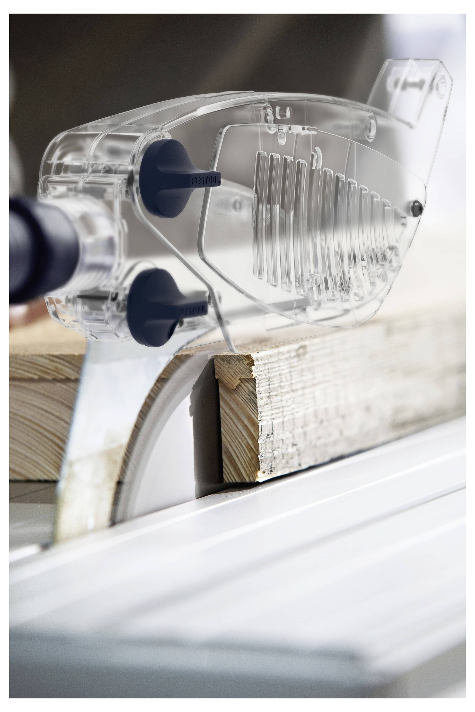 Eine Person verwendet einen Elektroschleiffer auf einem Holzbrett, mit einer sichtbaren Metallführungsschiene auf einem Tisch in einer Werkstattumgebung.