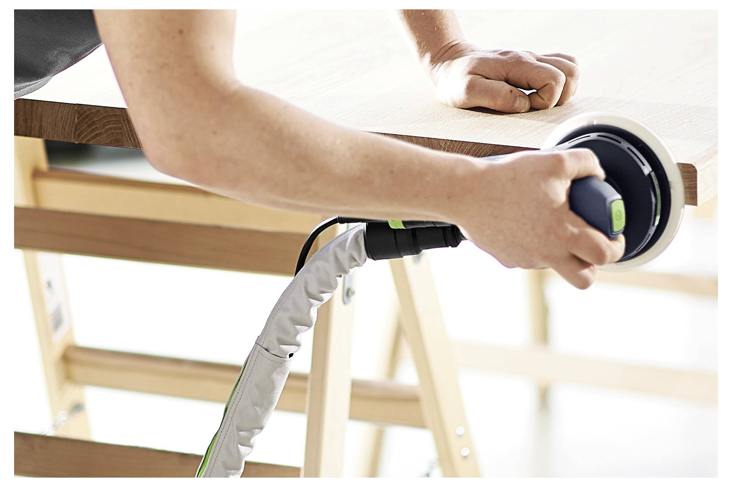 Eine Person schleift Holz auf einem Tisch mit einem elektrischen Schleiffer und konzentriert sich auf das Glätten der Oberfläche in einer Werkstattsumgebung.