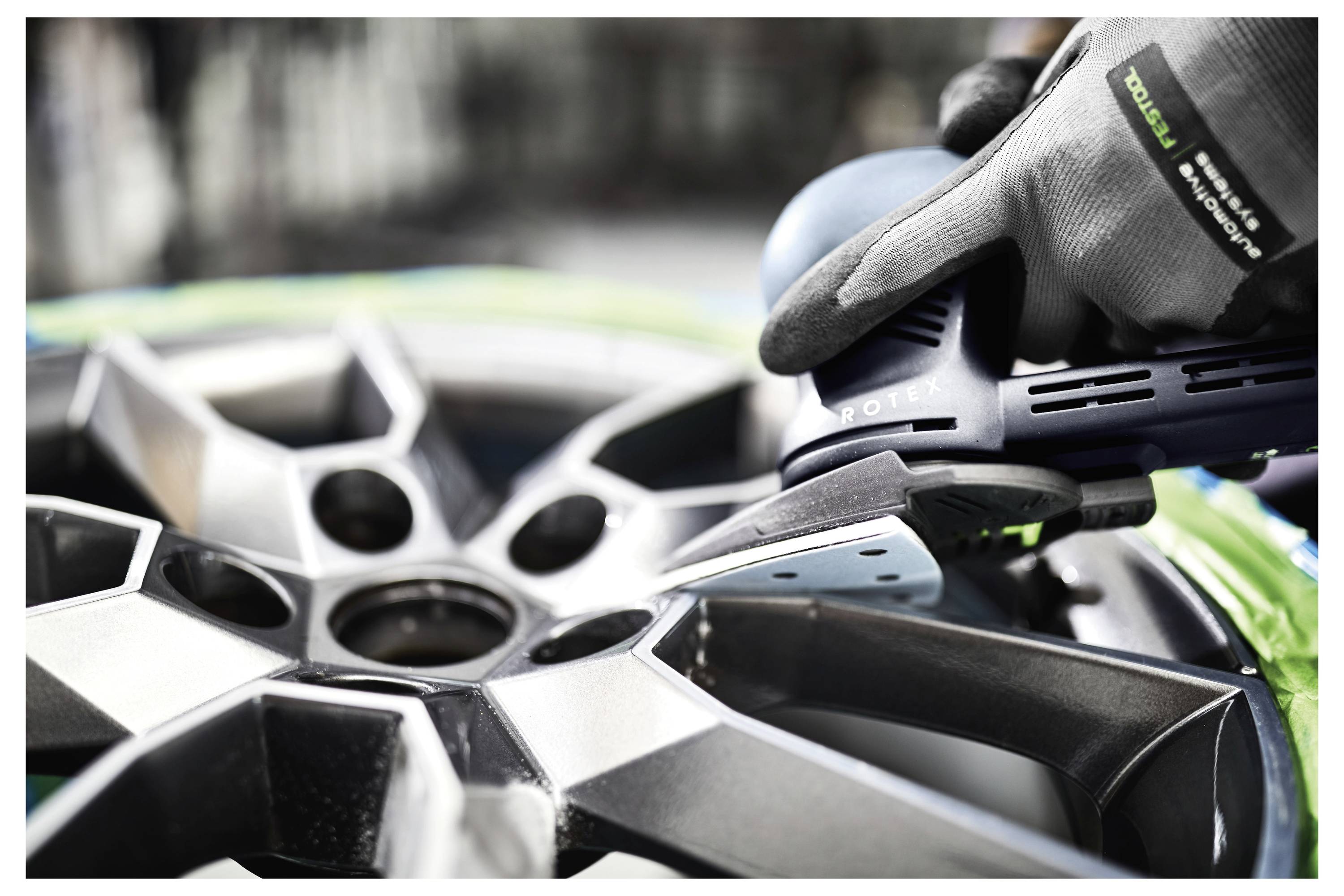 Eine Person verwendet ein Polierwerkzeug an einem silbernen Autrad, während sie Schutzhandschuhe trägt.