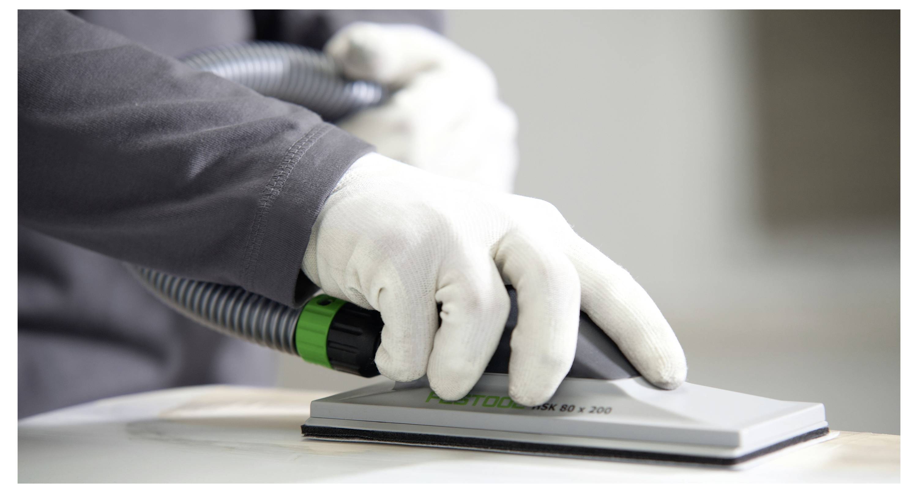 Nahaufnahme von Händen in weißen Handschuhen, die ein Elektroschleifergerät auf einer Holzoberfläche verwenden, mit Fokus auf Präzision und glatte Oberflächenfinish.