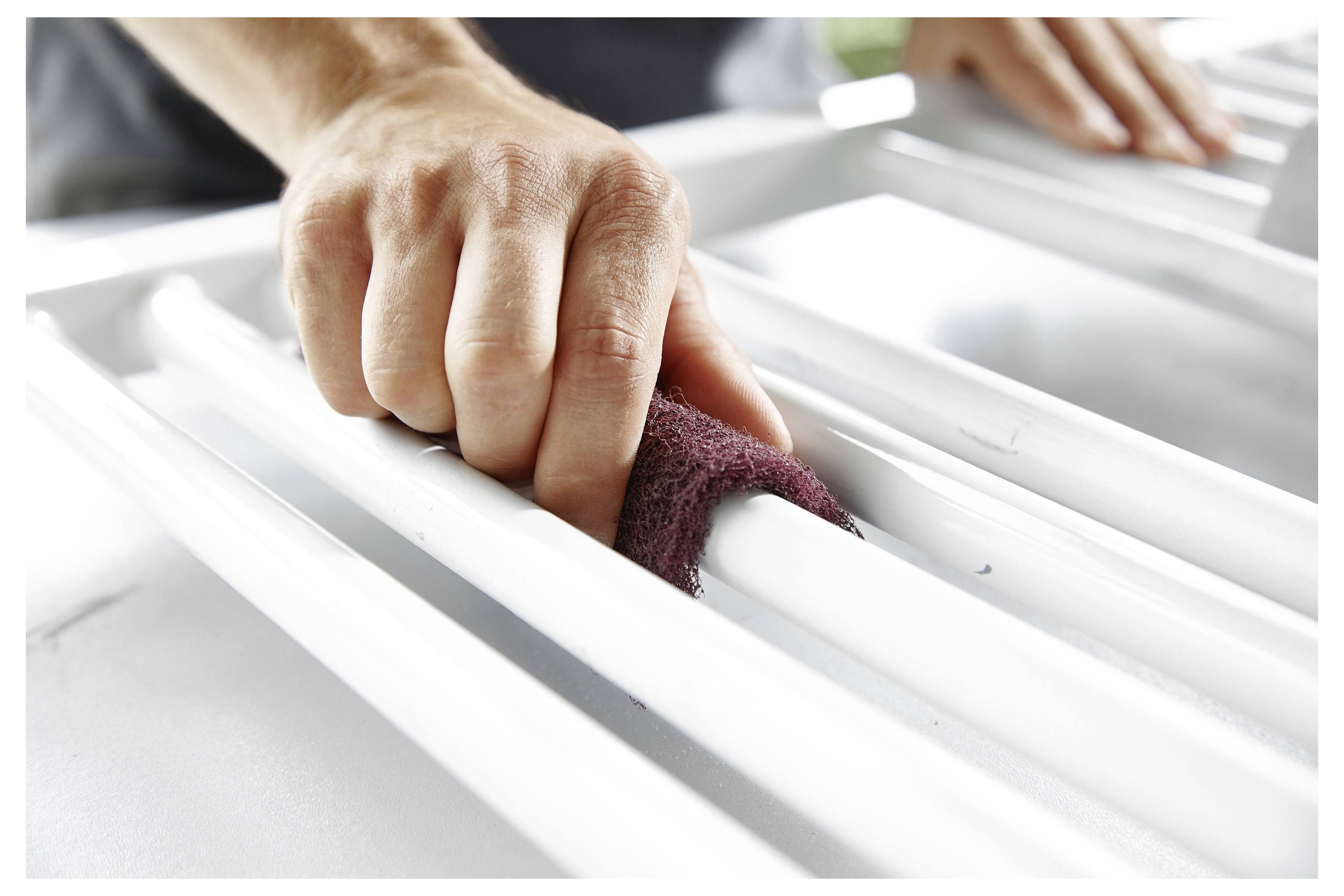 Eine Hand benutzt ein Schleifpad, um eine weiße Metallfläche zu glätten, mit Fokus auf Details und Präzision in einem hellen, gut beleuchteten Bereich.