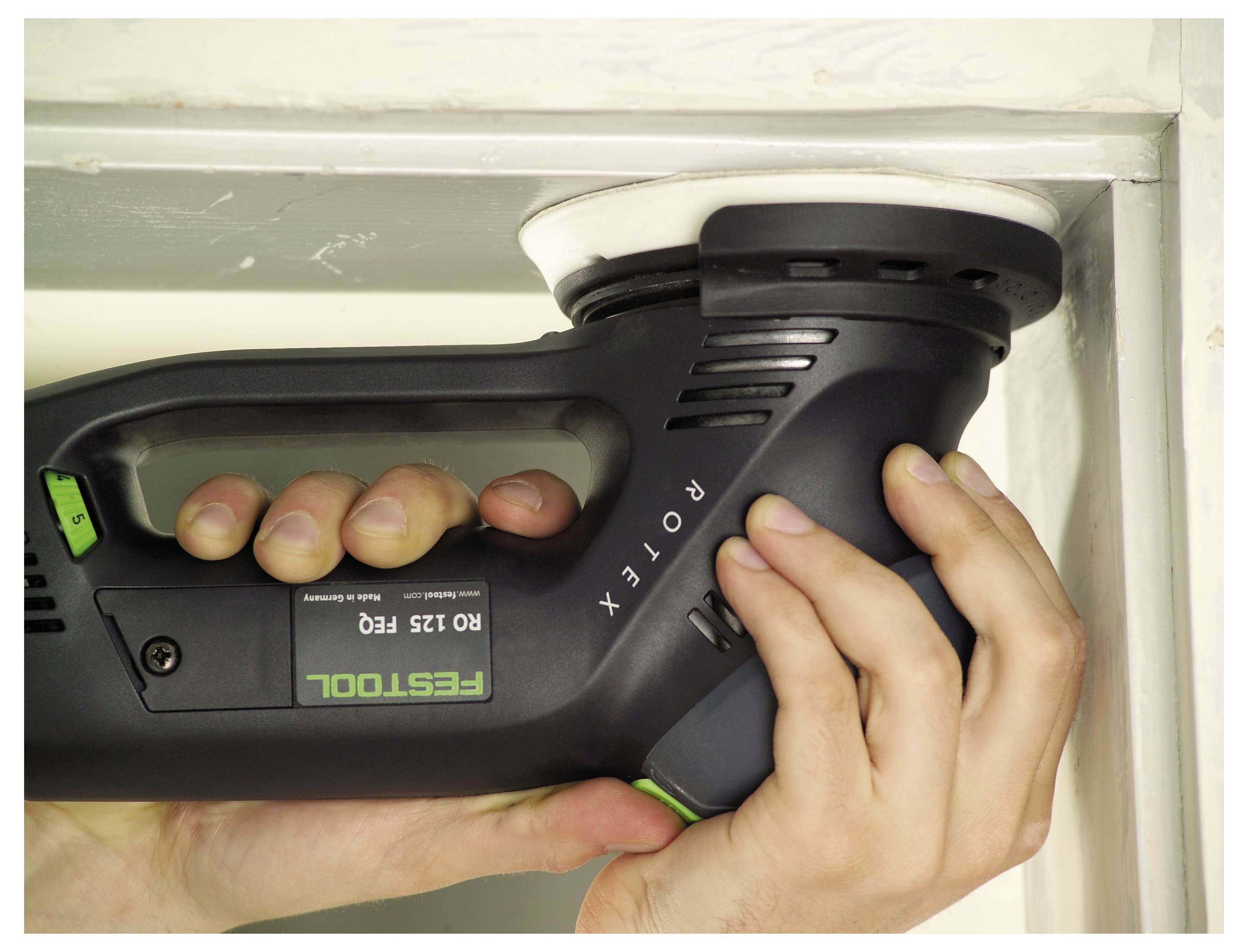 Person, die einen Festool ROTEX RO 125 FEQ Schleifer auf einer weißen Oberflächenkante verwendet, mit beiden Händen haltend, konzentriert sich auf präzises Schleifen.