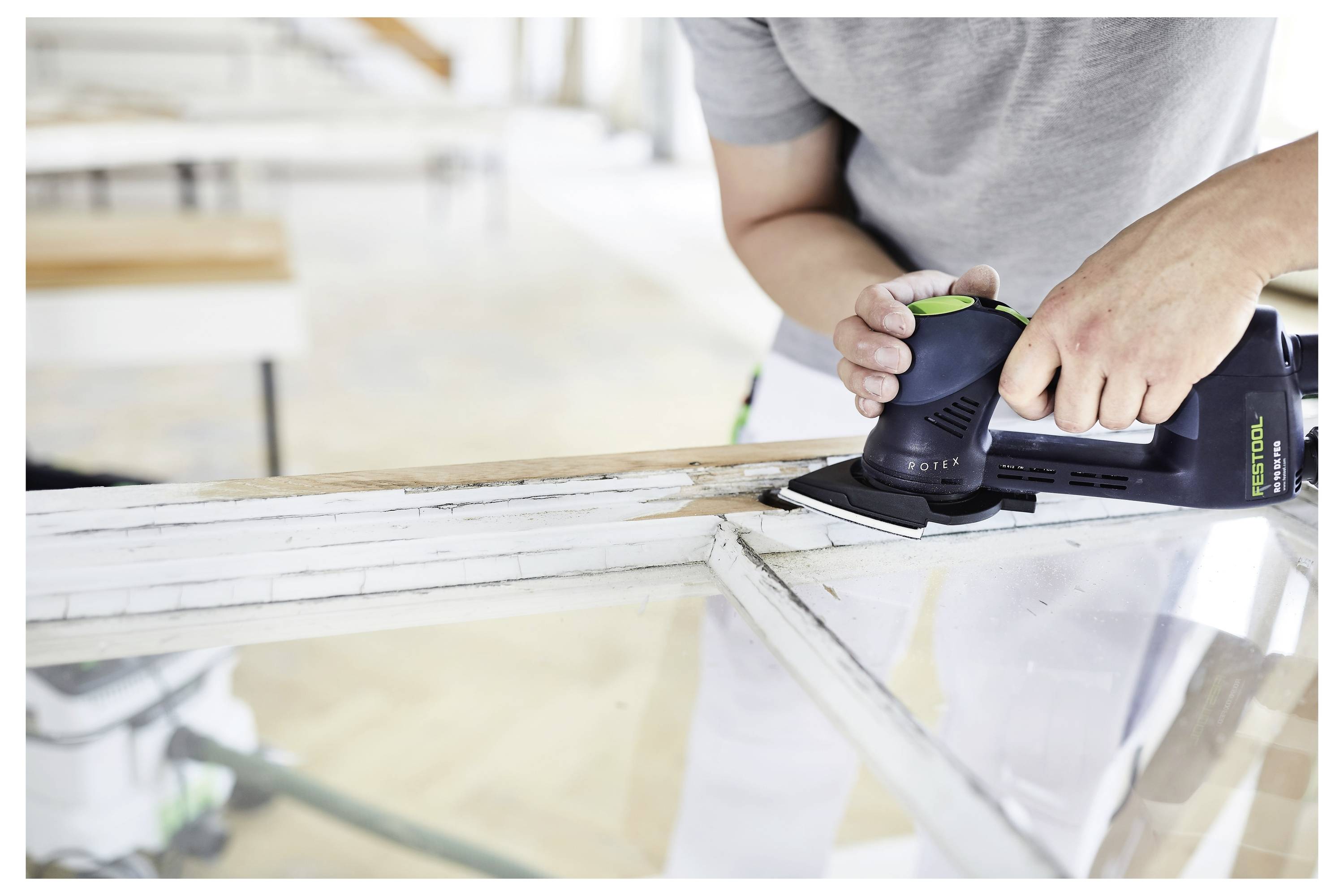 Eine Person benutzt einen Elektroschleiffer an der Kante eines Holzrahmens in Innenräumen und konzentriert sich auf die Ecken zum Glätten und Verfeinern.