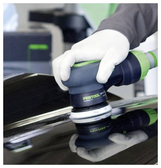 Eine behandschuhte Hand verwendet einen Festool-Poliermaschine auf einer glänzend schwarzen Oberfläche, die den Namen des Werkzeugs widerspiegelt. Die reflektierende Oberfläche ist unter der Poliermaschine sichtbar.