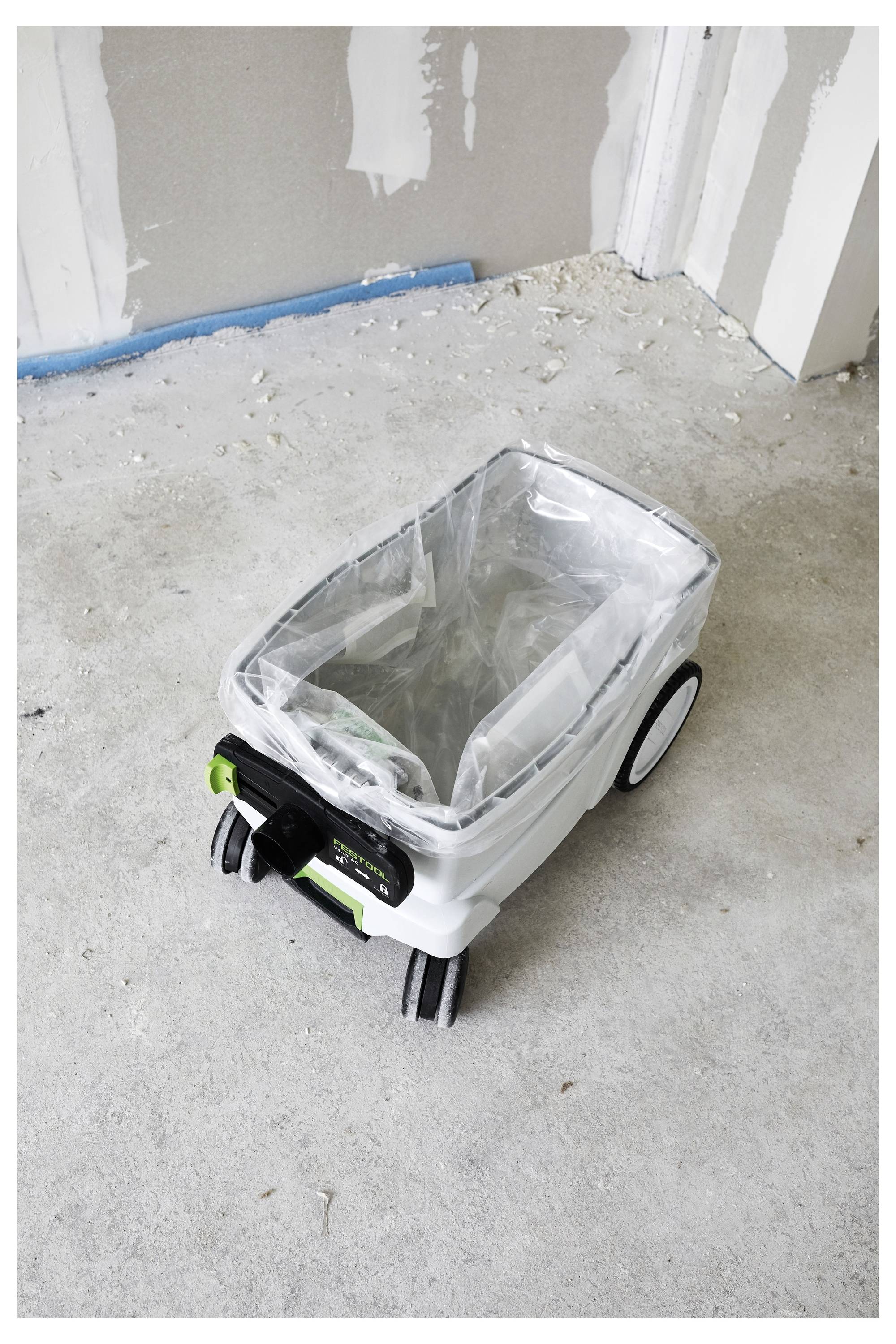 Ein Staubsauger ohne angebrachten Schlauch und Griff auf einem Betonboden eines unfertigen Zimmers mit sichtbaren Gipskartonwänden.