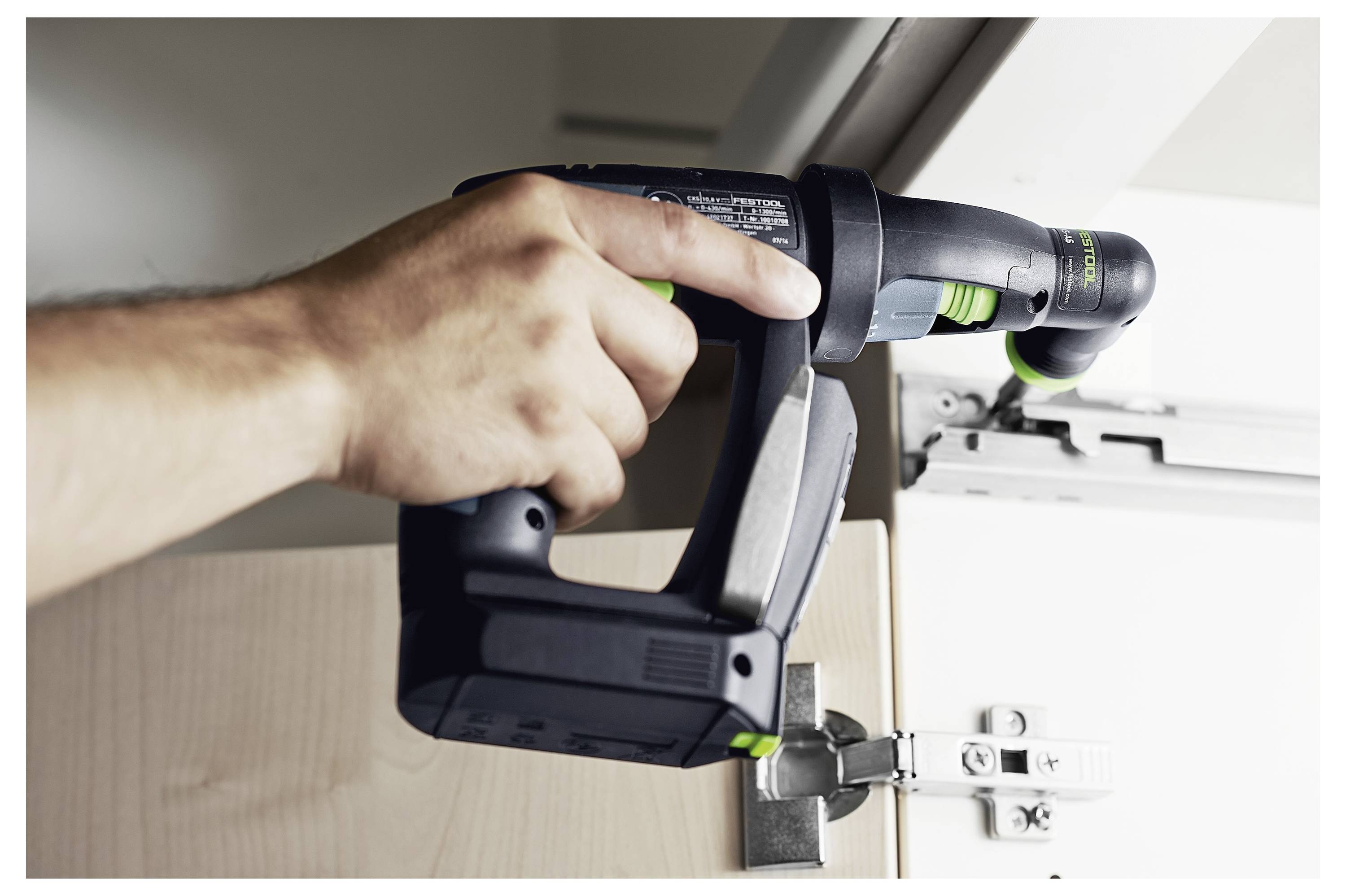 Eine Person benutzt einen Bohrer, um ein Schrankturnierscharnier anzupassen, was eine Heimwerkeraufgabe hervorhebt.