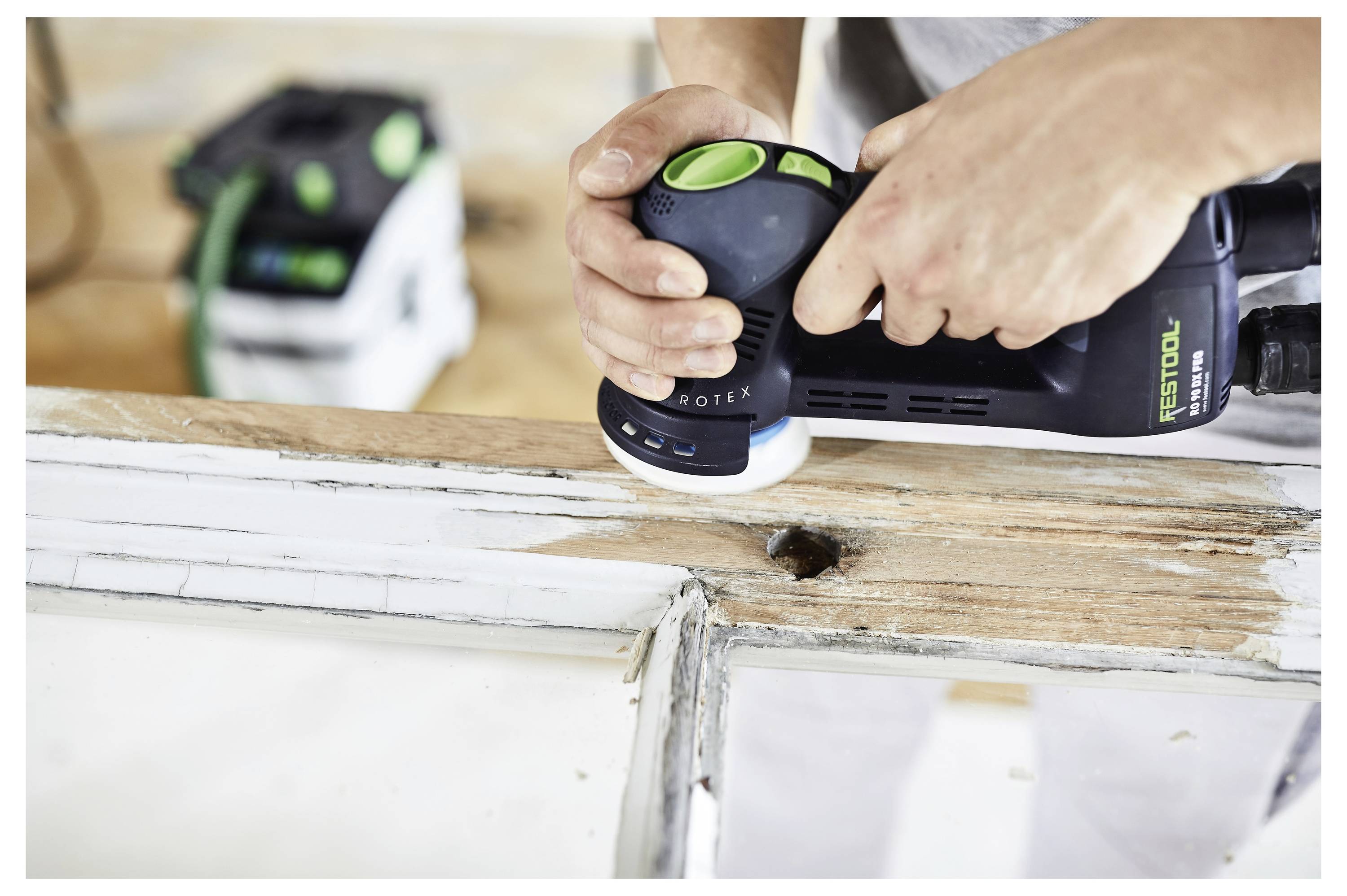 Eine Person benutzt einen elektrischen Elektroschleiffer, um einen Holzfensterrahmen zu glätten und alte Farbe zu entfernen und die Oberfläche zu glätten.