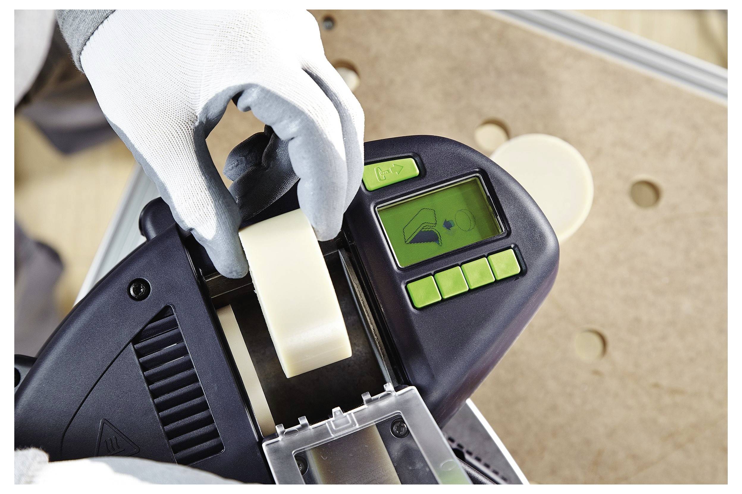 „Person, die eine Maschine zum Aufkleben von Band benutzt, trägt Schutzhandschuhe. Das Display zeigt ein Setup-Symbol, die Knöpfe sind grün, hält eine Rolle Band.