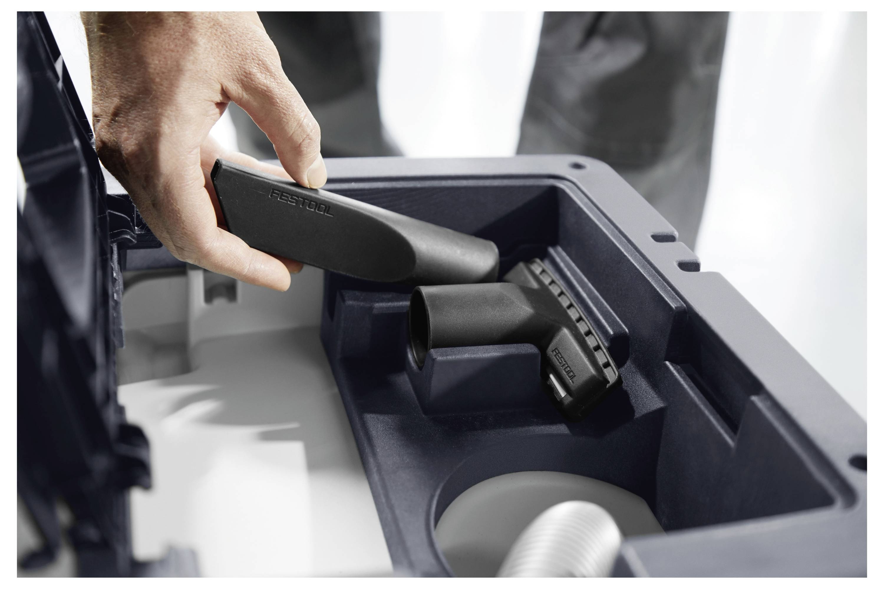 Eine Hand, die eine Düse in ein Fach eines Staubsaugers einführt, wobei die Lagerung oder Organisation von Zubehörteilen hervorgehoben wird.