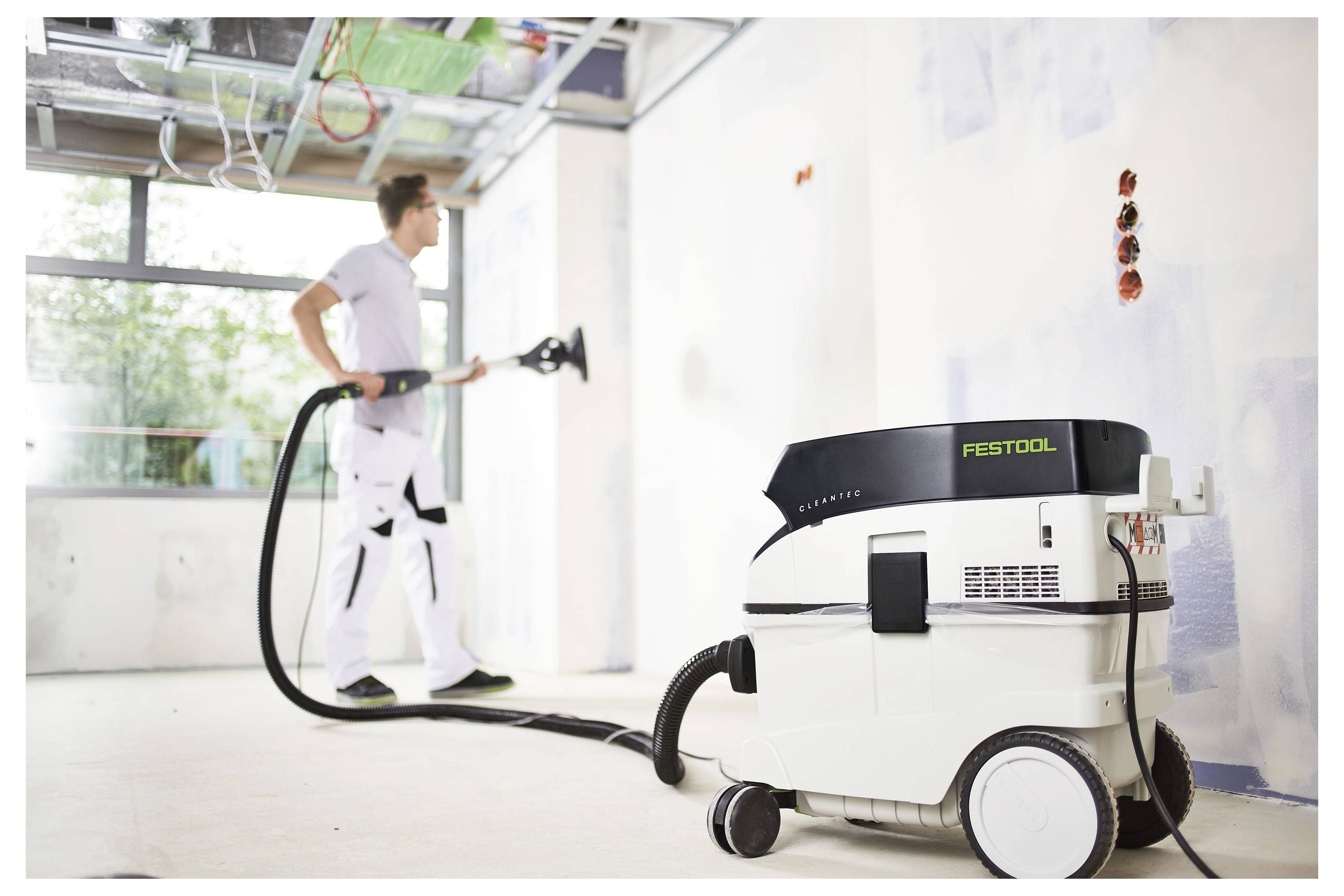 Eine Person mit Handschuhen und Arbeitshose benutzt ein Elektrowerkzeug, um in eine Oberfläche in einem teilweise renovierten Raum mit freiliegenden Ziegelwänden zu bohren.