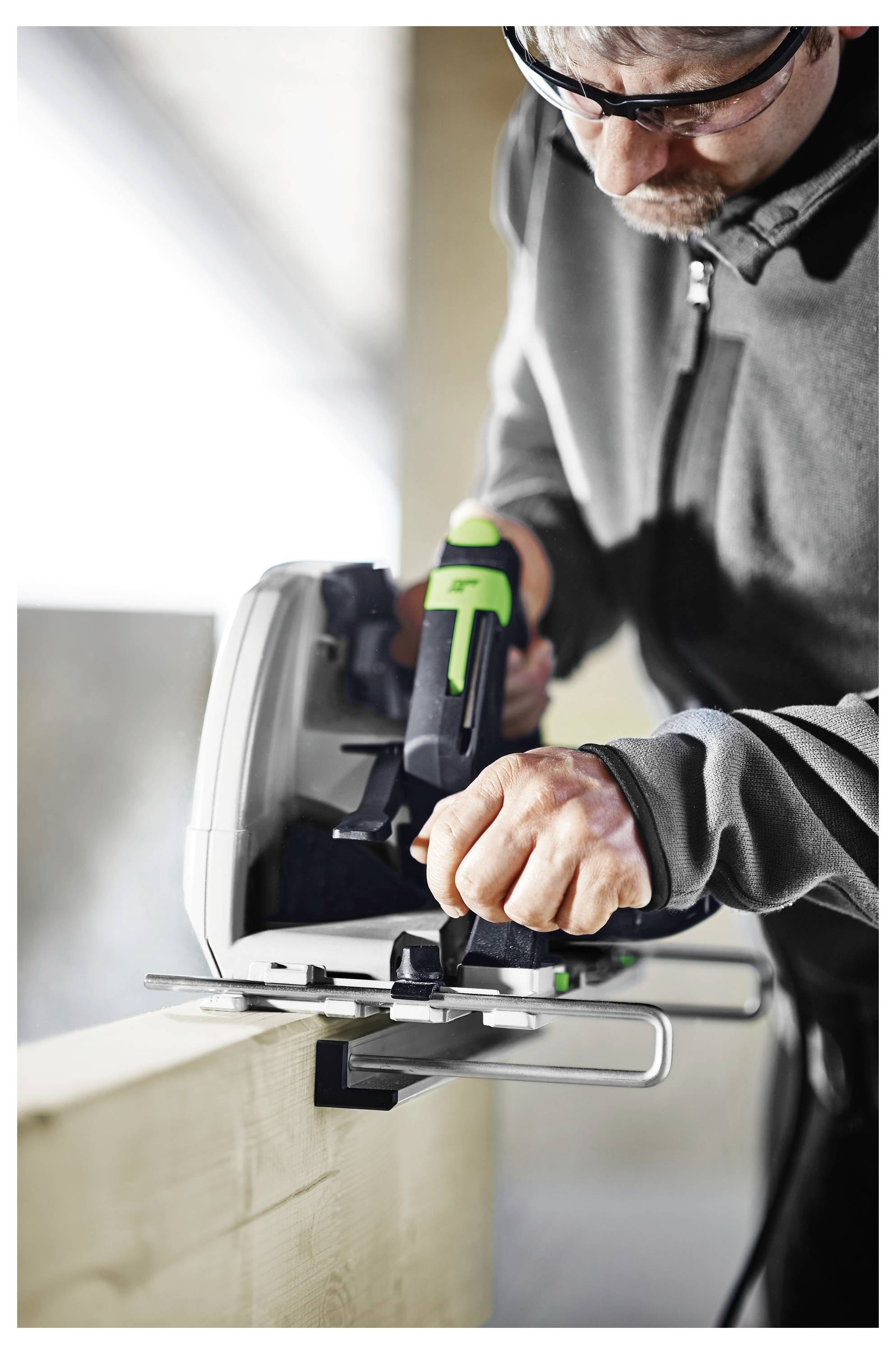 Person, die einen Elektroschleiffer auf einer Holzoberfläche verwendet, konzentriert sich auf das Glätten der Kante. Die helle, gut beleuchtete Umgebung deutet auf eine Werkstattumgebung hin.