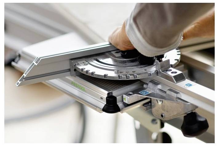 Eine Hand stellt den Winkel einer Gehrungssäge ein und konzentriert sich auf einen präzisen Schnitt. Die Einstellungsskala des metallischen Werkzeugs ist sichtbar und zeigt feine Details.