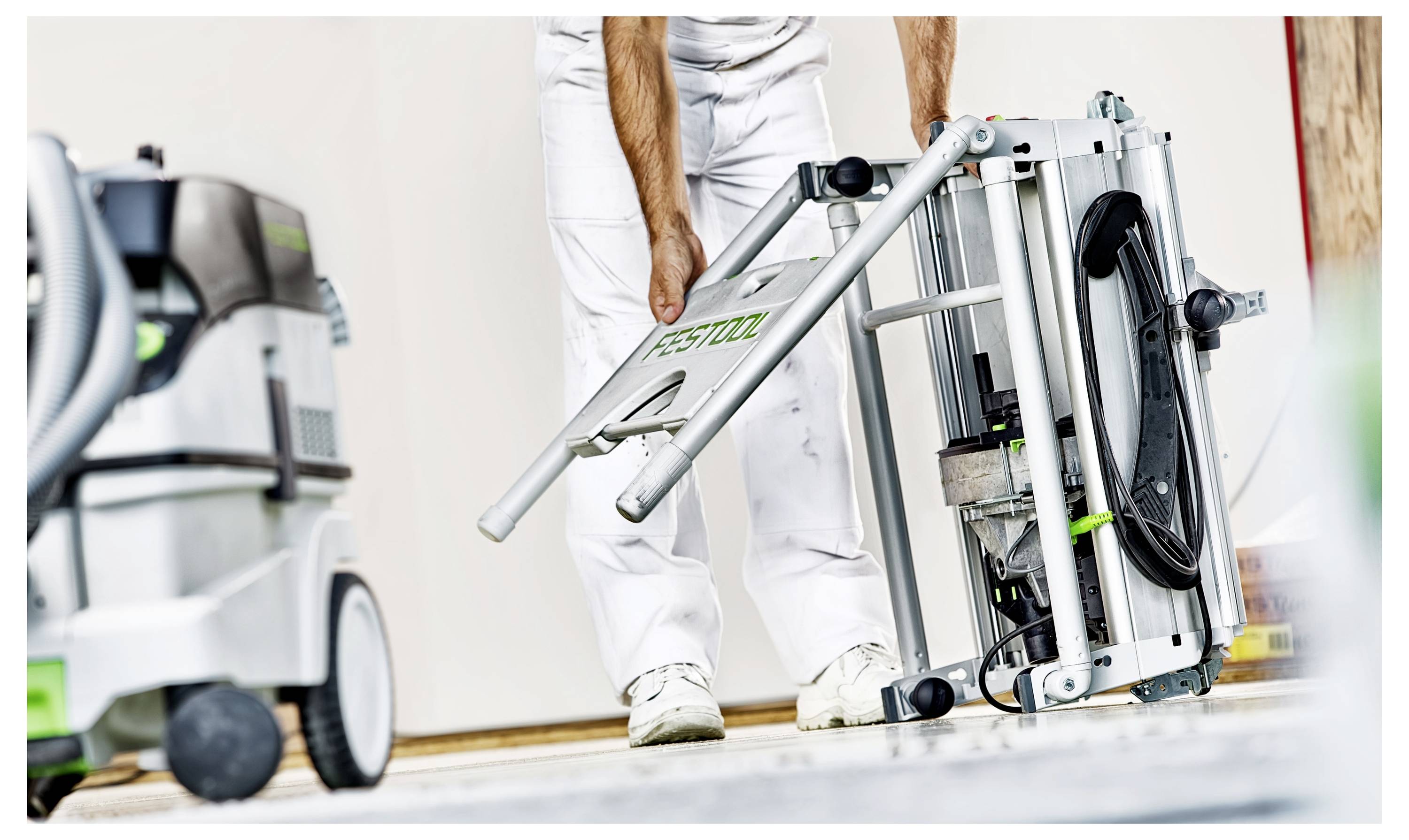 A person in work attire sets up industrial equipment, with a focus on a power tool featuring the brand logo, beside a vacuum system.