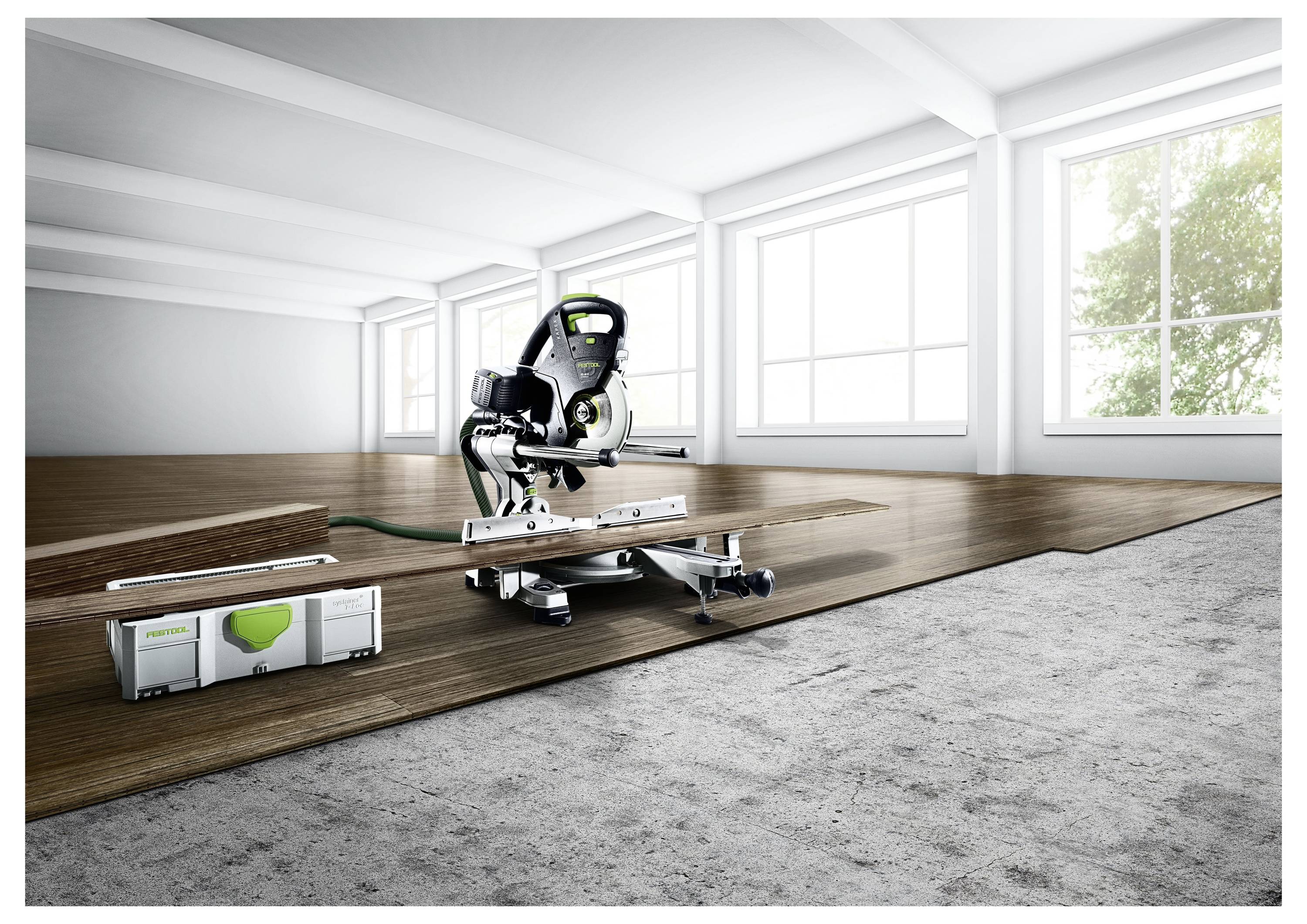 Eine Gehrungssäge auf einem Ständer in einem hellen, geräumigen Raum. Sie ist über teilweise verlegtem Holzfußboden positioniert, mit einer Werkzeugkiste in der Nähe.