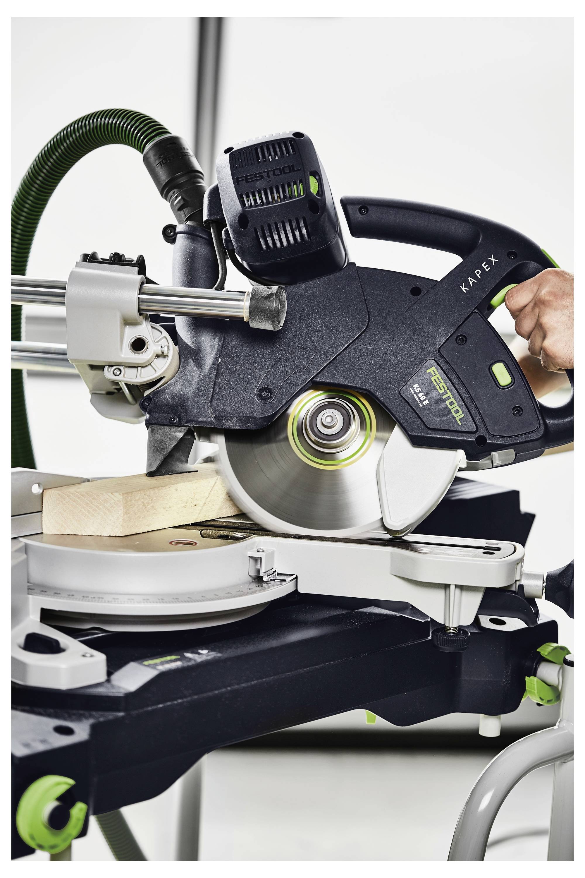 Eine Kreissäge schneidet ein Stück Holz auf einer Werkbank, mit einem sichtbaren Bediengriff und einem angeschlossenen Staubsammelschlauch.