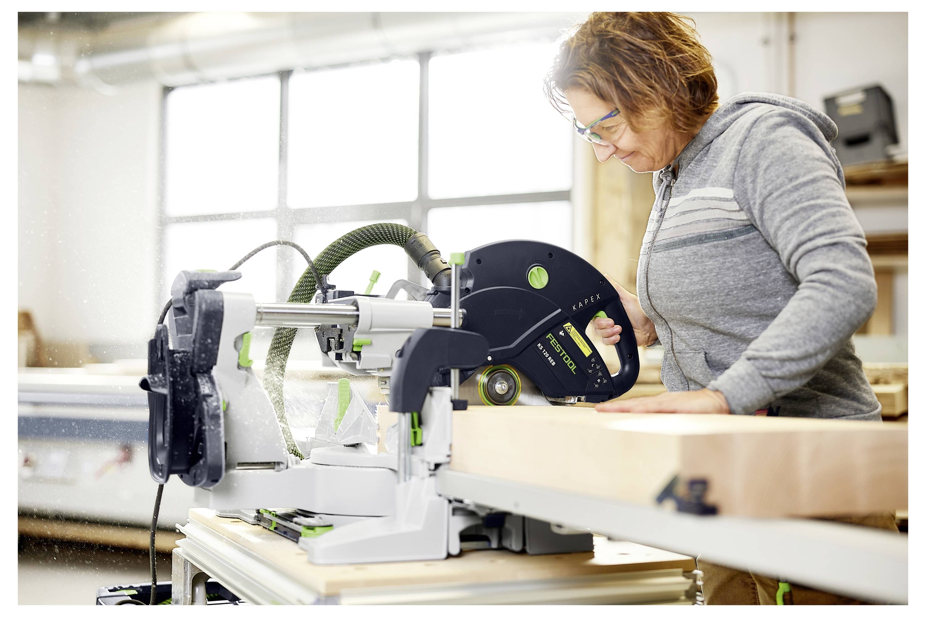 Eine Person in einem grauen Hemd benutzt eine kabellose Elektrobohrmaschine in einer Werkstatt und konzentriert sich darauf, einen Bohraufsatz anzubringen.