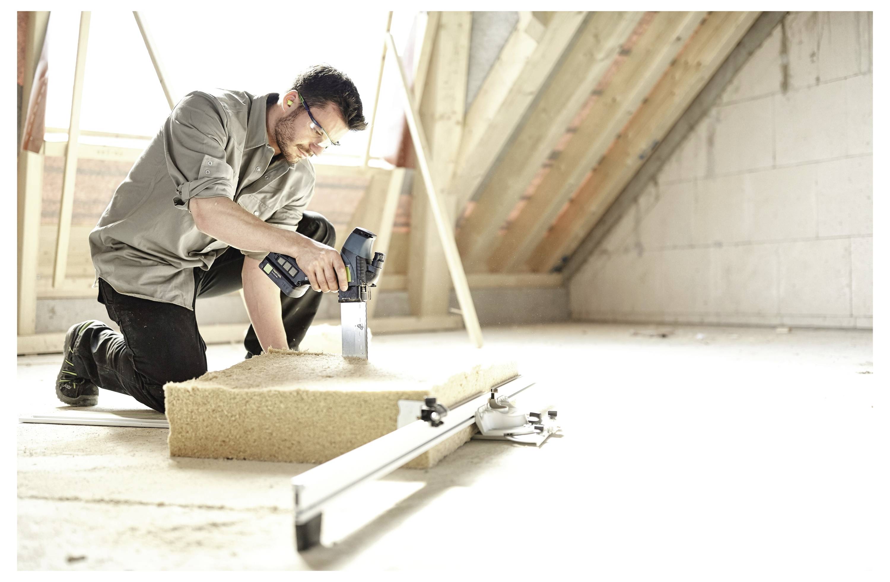 Eine Person, die Schutzhandschuhe trägt, benutzt ein Elektrowerkzeug auf einer Baustelle, wobei Ausrüstung und ein Betonboden sichtbar sind.