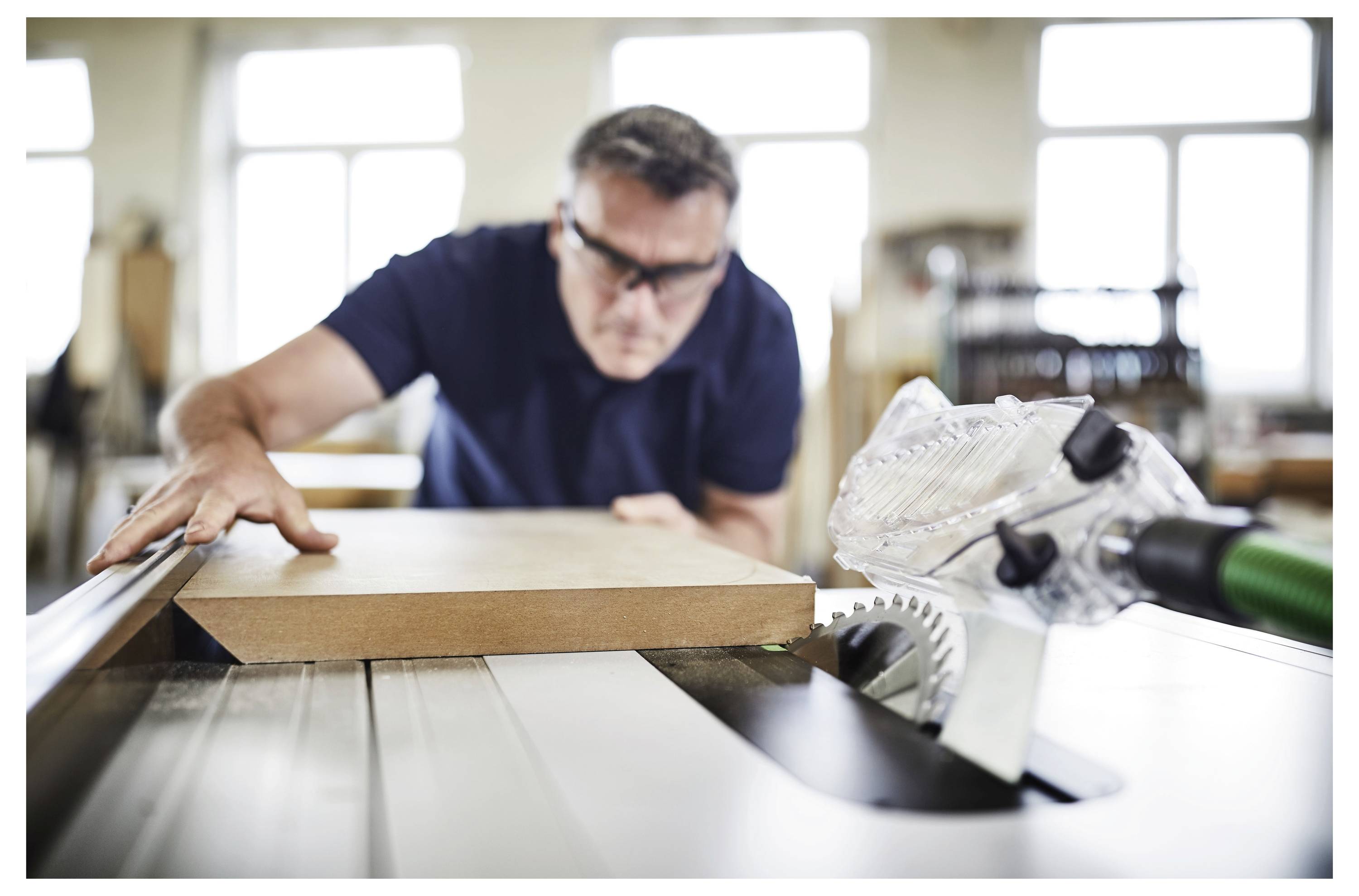 Eine Person in einer Werkstatt schneidet Isolationsmaterial mit einer tragbaren Säge zu und bereitet es für die Installation vor. Holzbalken und unvollendete Wände sind sichtbar.