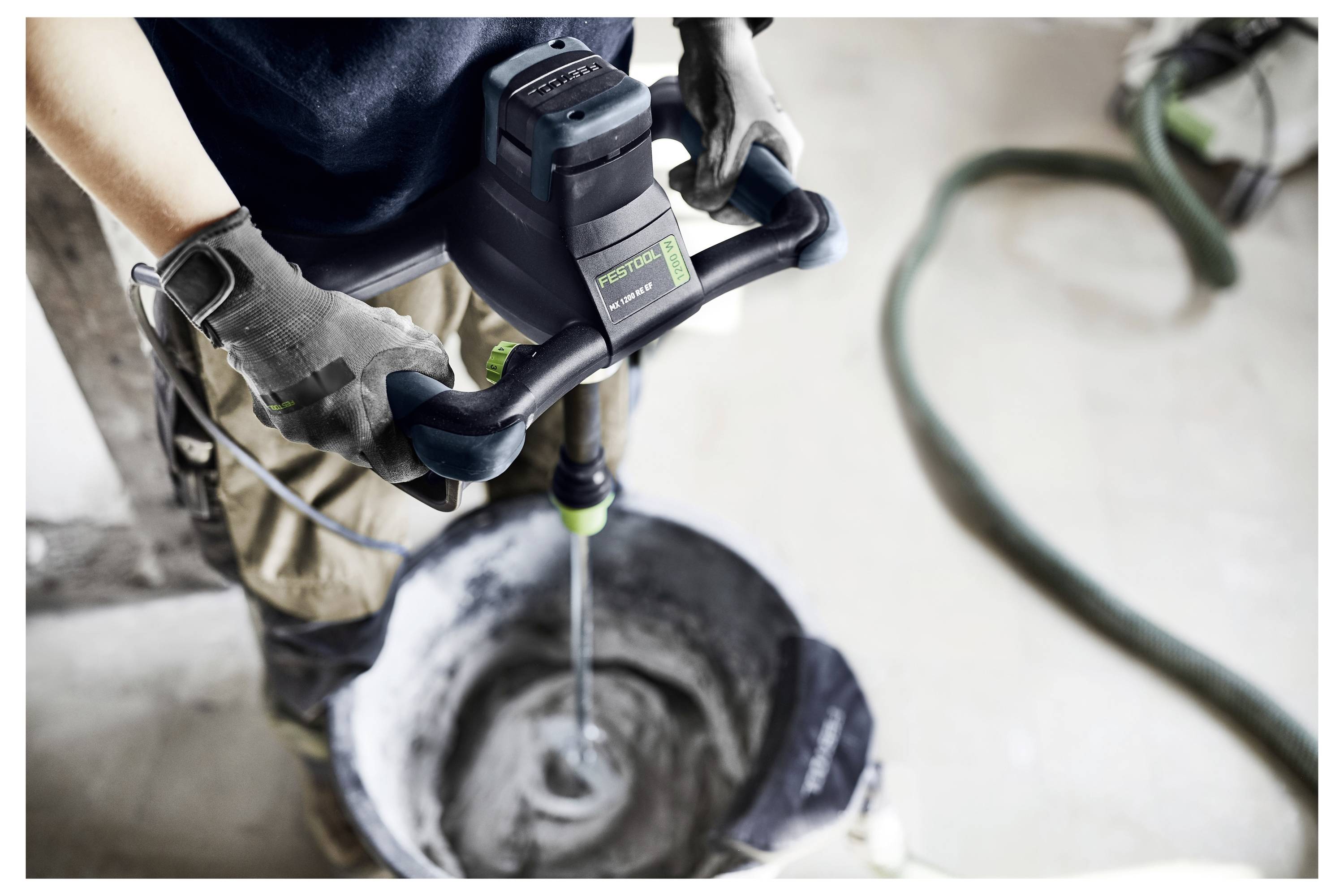 Eine Person in Arbeitskleidung nutzt eine Festool Elektrobohrmaschine mit einem großen Bohrer, um in eine weiße Ziegelmauer zu bohren, was auf eine Baustelle hinweist.