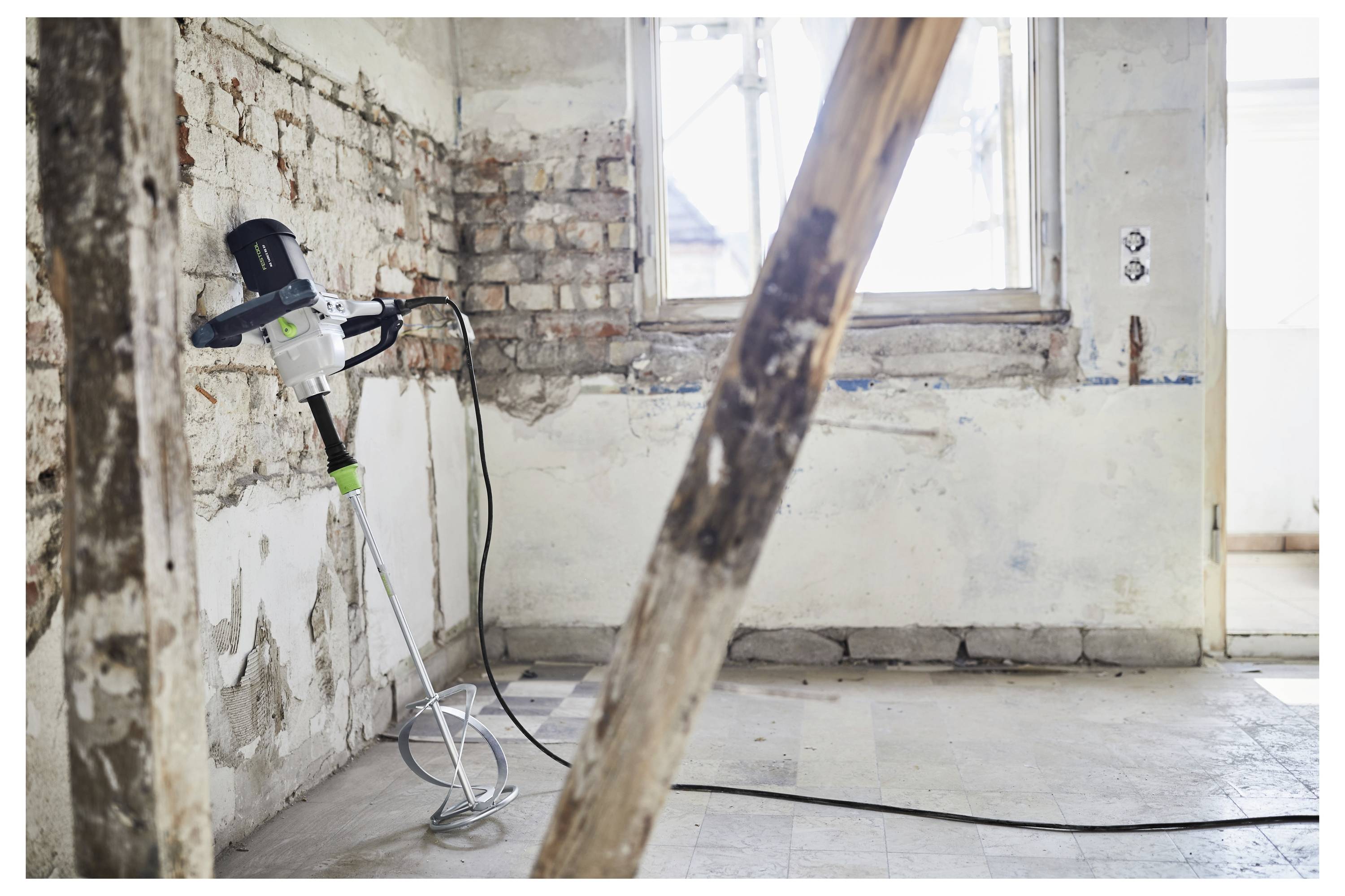 Ein leeres Zimmer unter Renovierung mit freiliegenden Ziegelmauern und einer Betonmischmaschine, die an der Wand lehnt. Sonnenlicht fällt durch das Fenster herein.