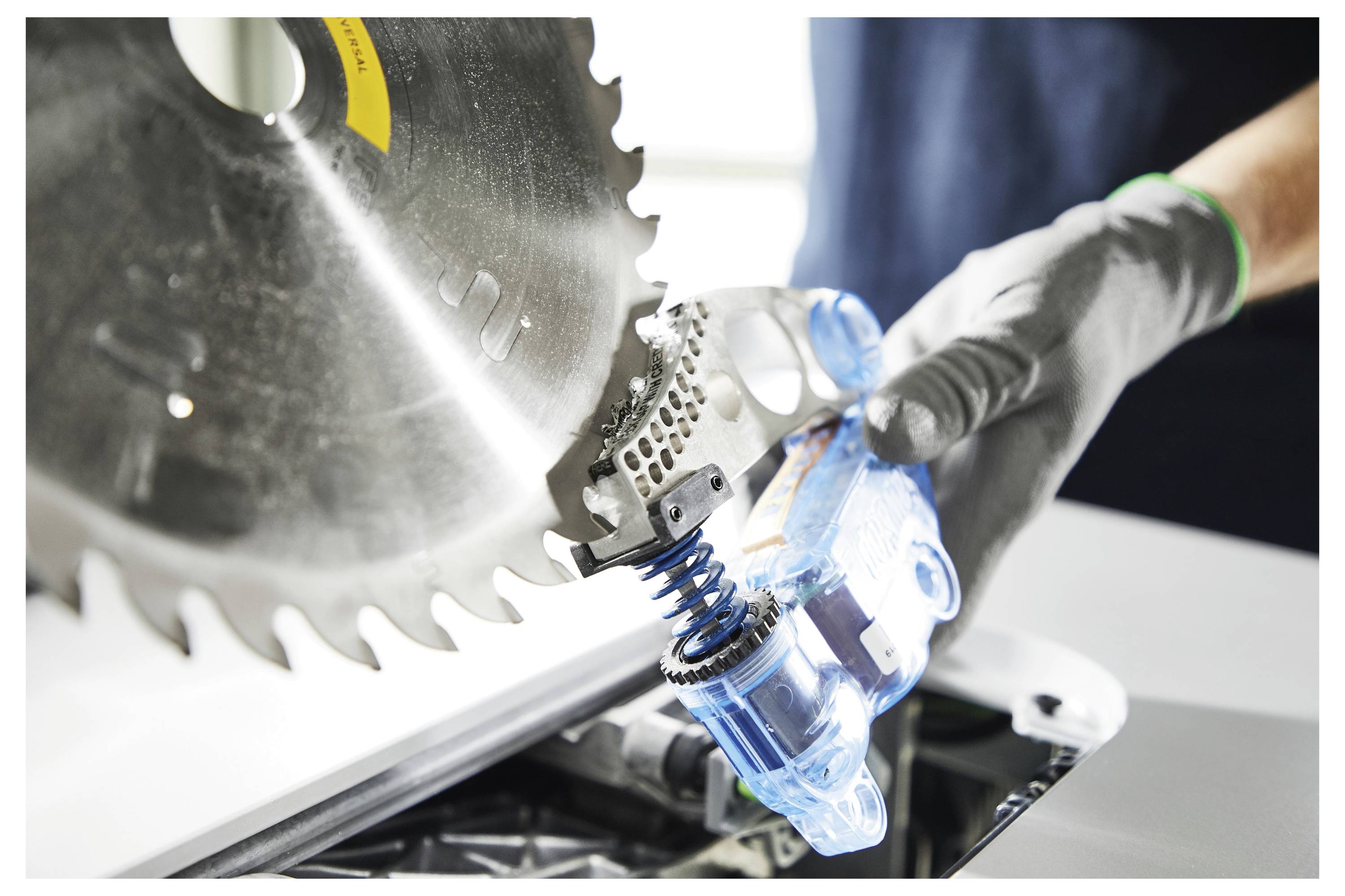 Eine Person, die Handschuhe trägt, benutzt eine Kreissäge, um einen Gegenstand zu schneiden. Der Fokus liegt auf dem Sägeblatt, das auf den Gegenstand trifft, wobei die Aktion betont wird.