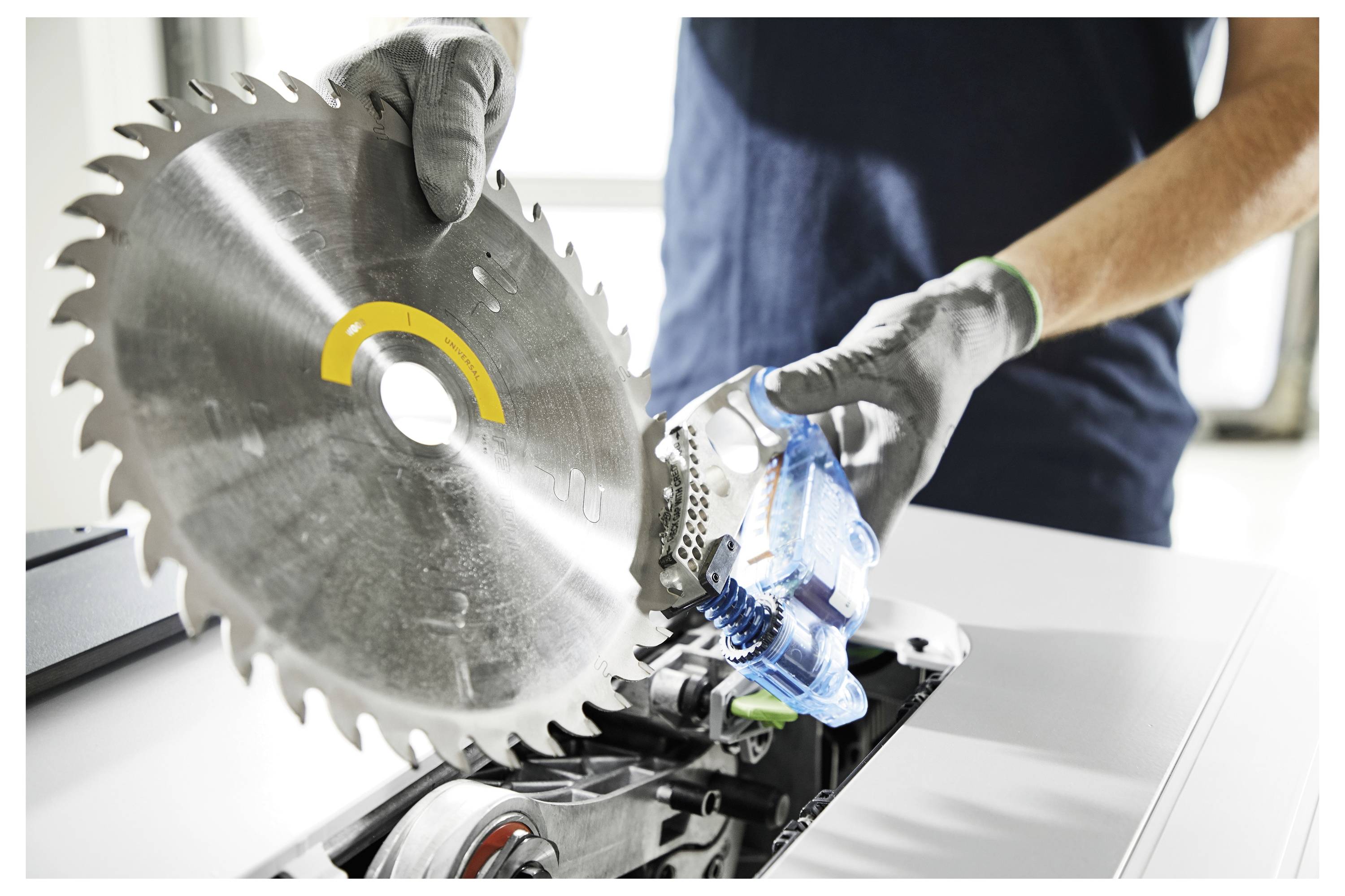 Eine Person, die Schutzhandschuhe trägt, installiert ein großes Kreissägeblatt in eine Sägenmaschine und demonstriert so die ordnungsgemäße Ausrüstungseinrichtung.