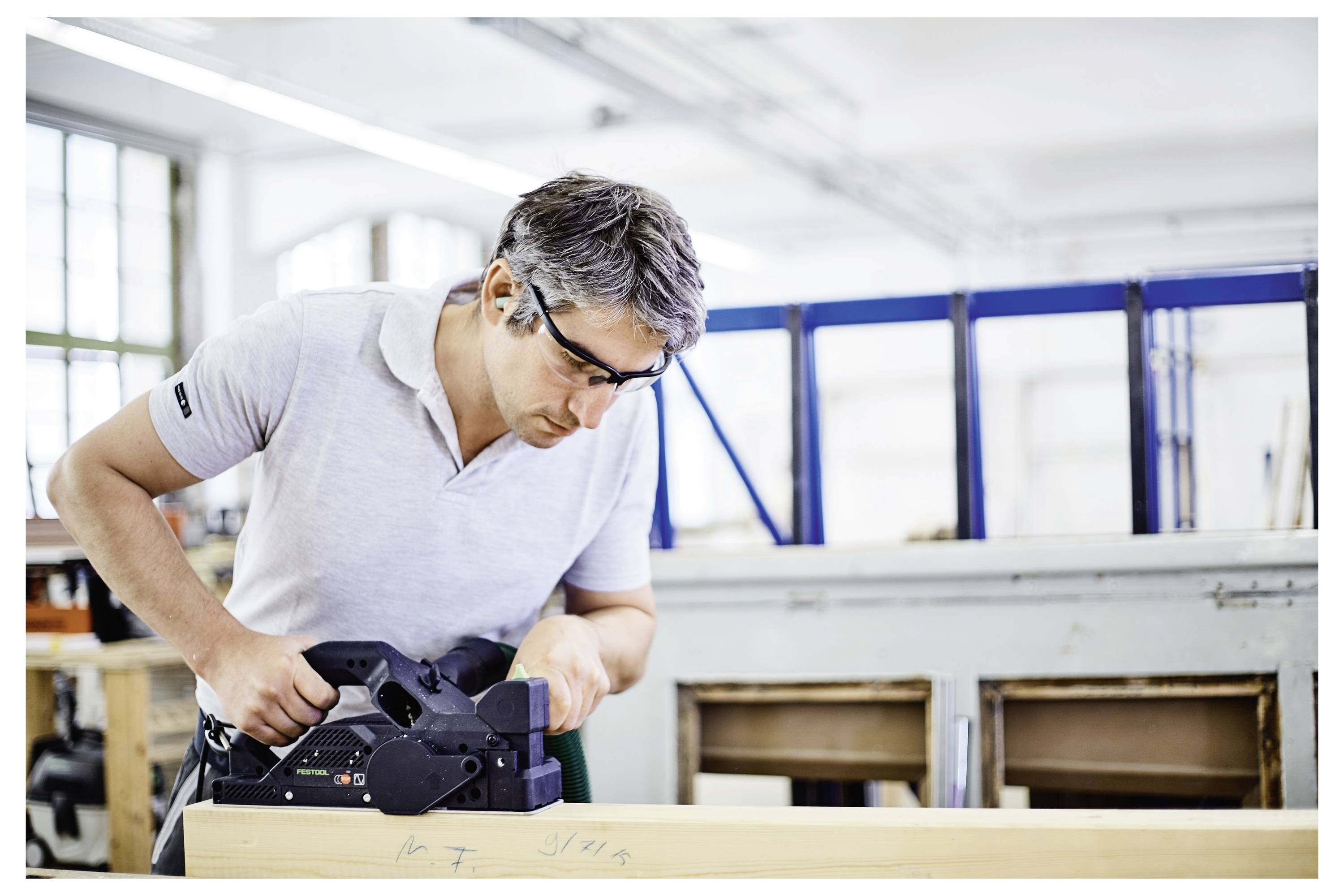 Eine Person mit Schutzbrille bedient eine Holzbearbeitungsmaschine in einer Werkstatt und konzentriert sich dabei auf Präzision und sorgfältige Handwerkskunst.