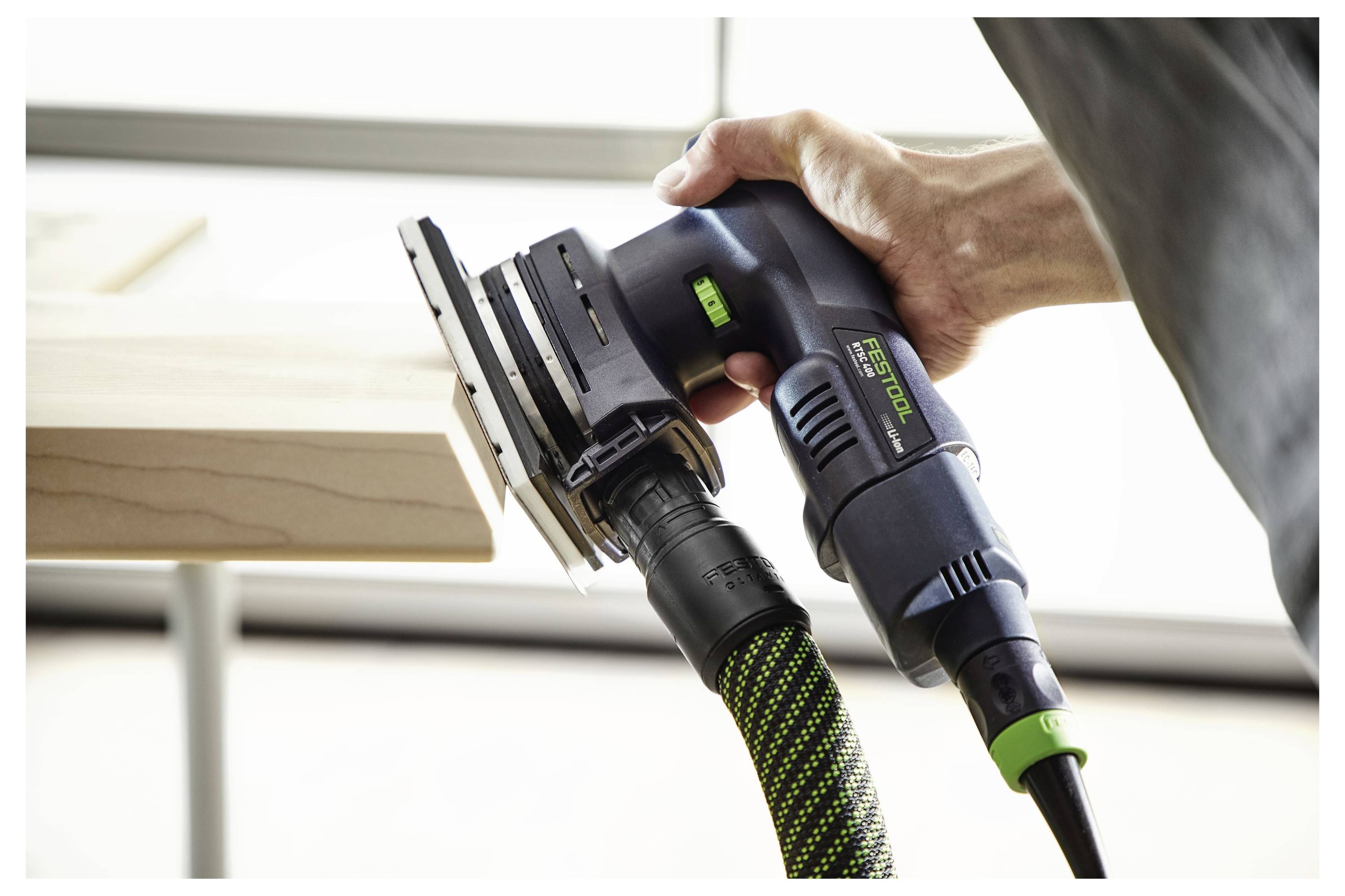 Eine Person, die einen Elektroschleiffer auf einer Holzoberfläche verwendet, wobei der Fokus auf der Schleifwirkung des Werkzeugs liegt.