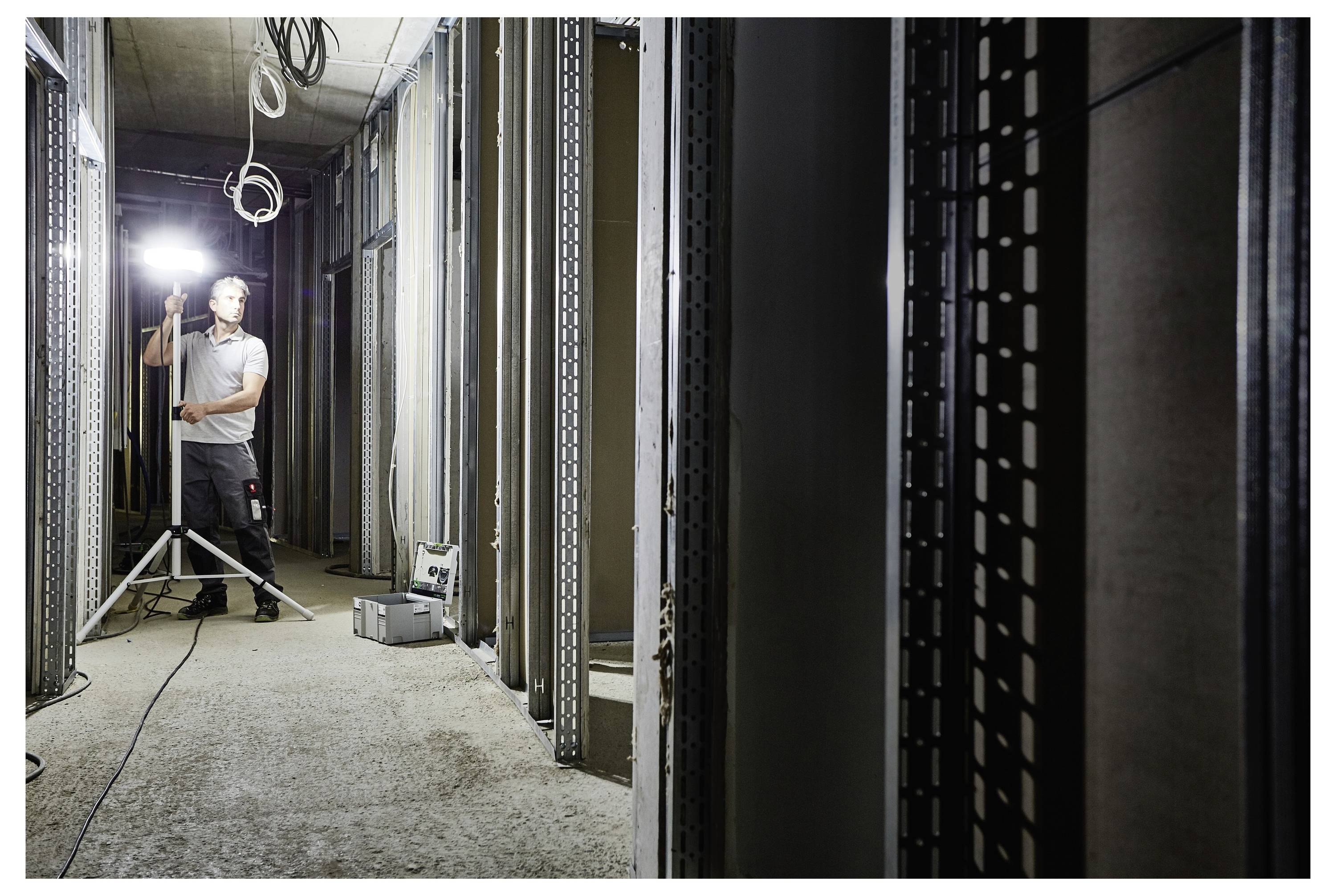 Ein Mann, der Schutzbrille trägt, benutzt eine Tischkreissäge, um ein Stück Holz in einer Werkstatt zu schneiden. Der Raum ist mit Holzbearbeitungswerkzeugen gefüllt.