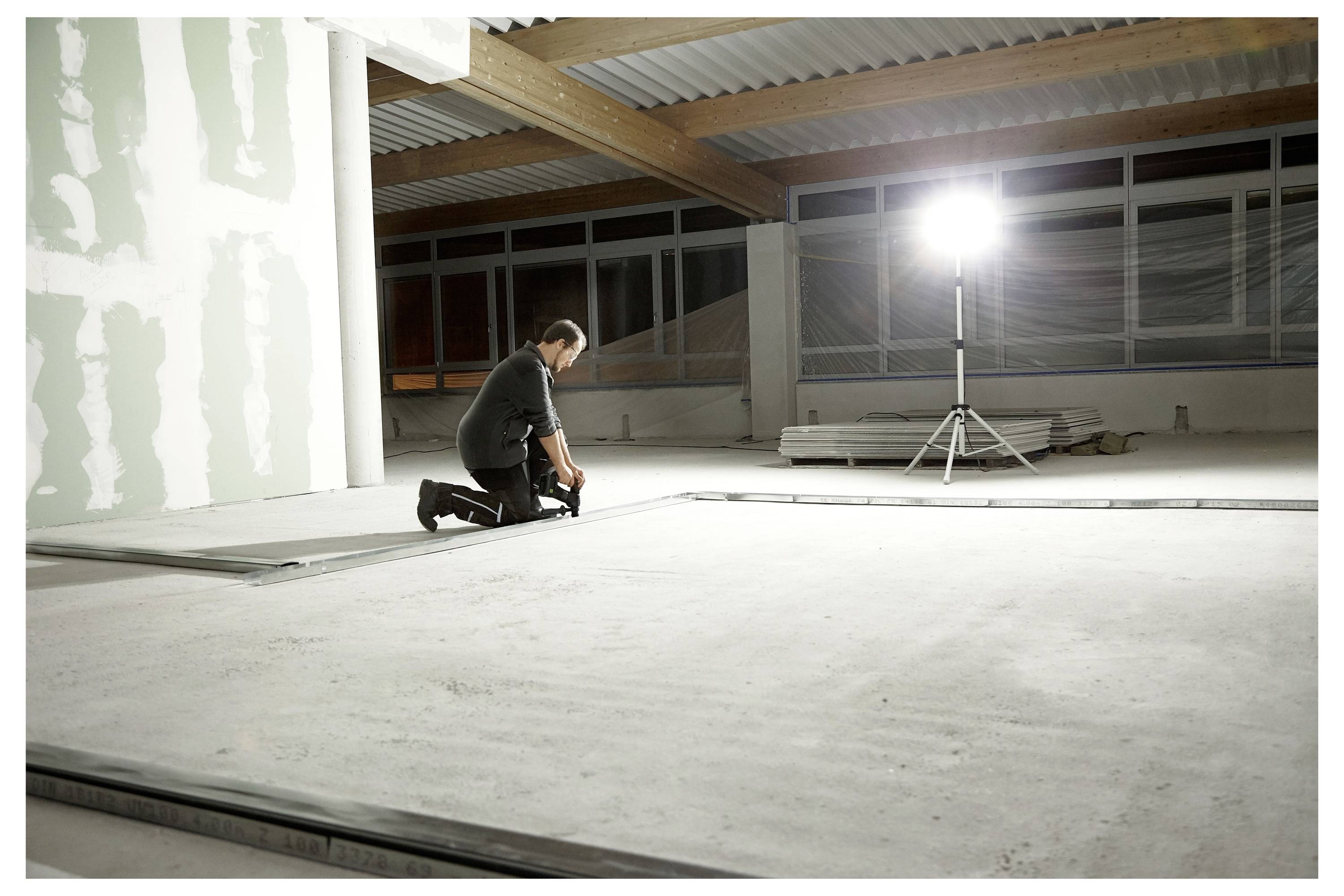 Ein Mann mit Gehörschutz und Schutzbrille benutzt ein Elektrowerkzeug, um dicke Isolierungsplatten auf einer gut beleuchteten Baustelle zu schneiden.