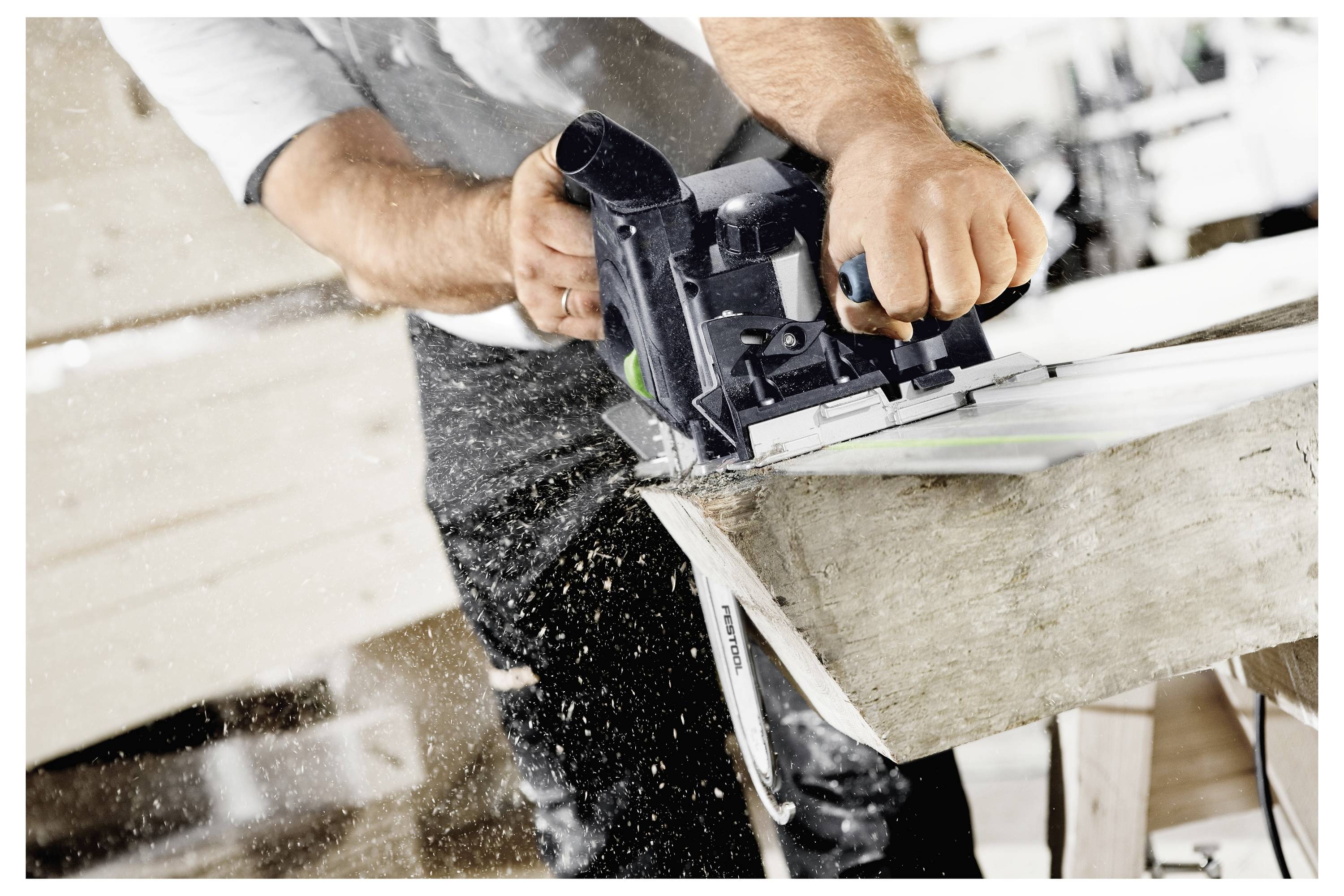 Eine Person trägt eine große weiße Schachtel eine Holztreppe in einer industriellen Umgebung hinauf, trägt eine Mütze und Arbeitskleidung.