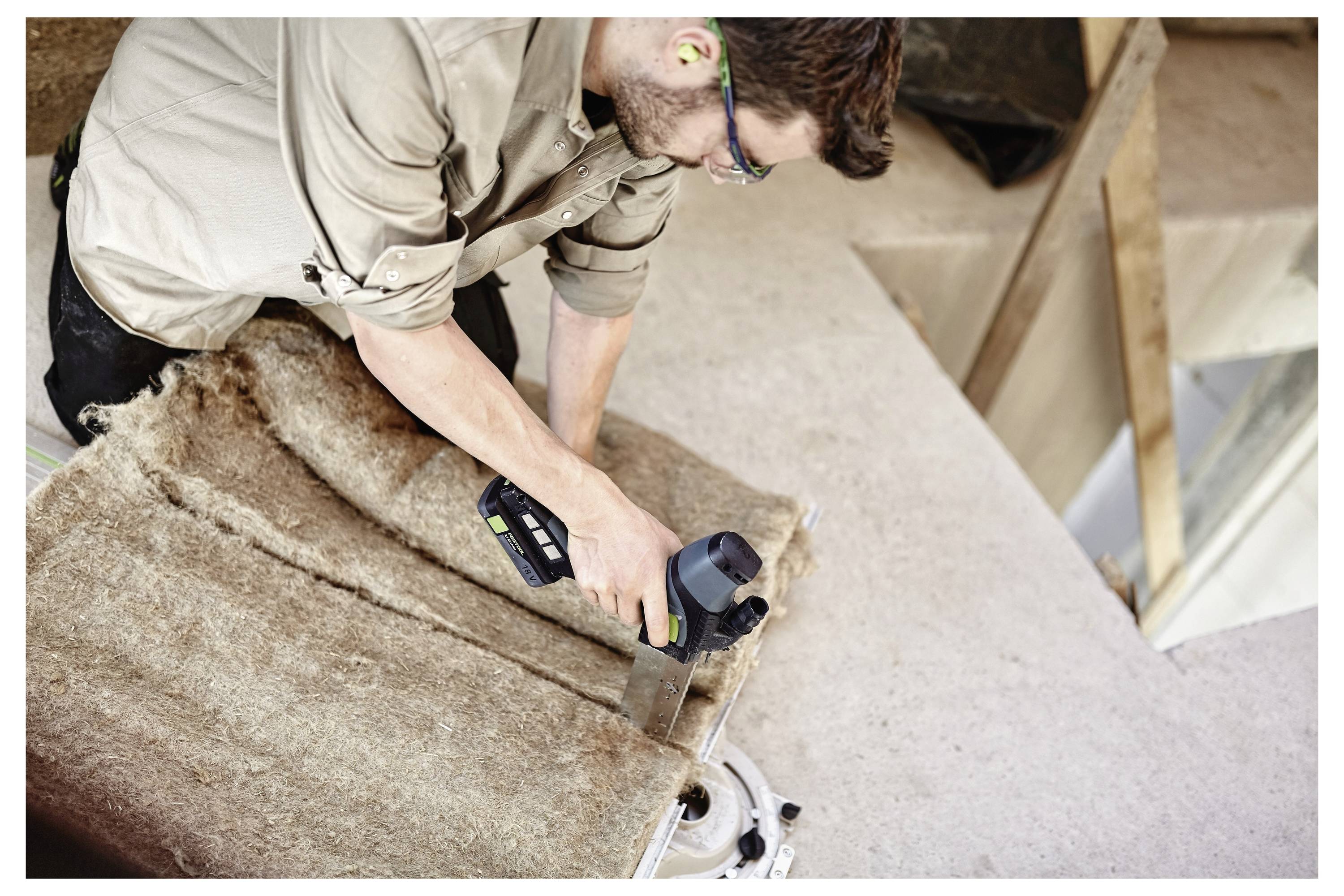Ein Mann mit Schutzbrille und traditioneller Weste benutzt einen Akku-Bohrer, um ein Loch in eine Holzplatte zu bohren.