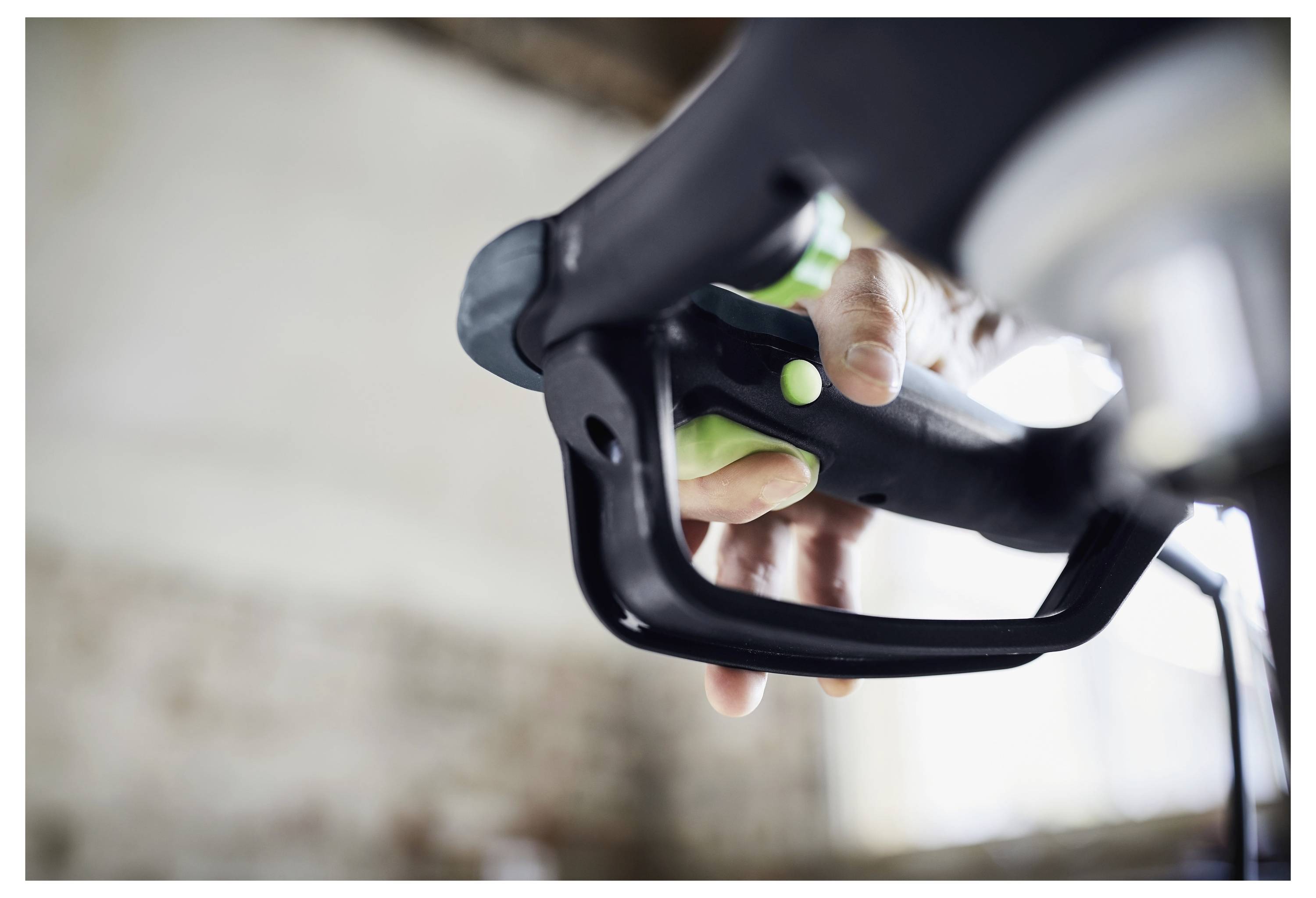 Eine Person ergreift einen schwarzen Griff einer Elektrobohrmaschine und konzentriert sich auf die Kontrolle. Der Hintergrund ist verschwommen und deutet auf eine Innenbaustelle hin.