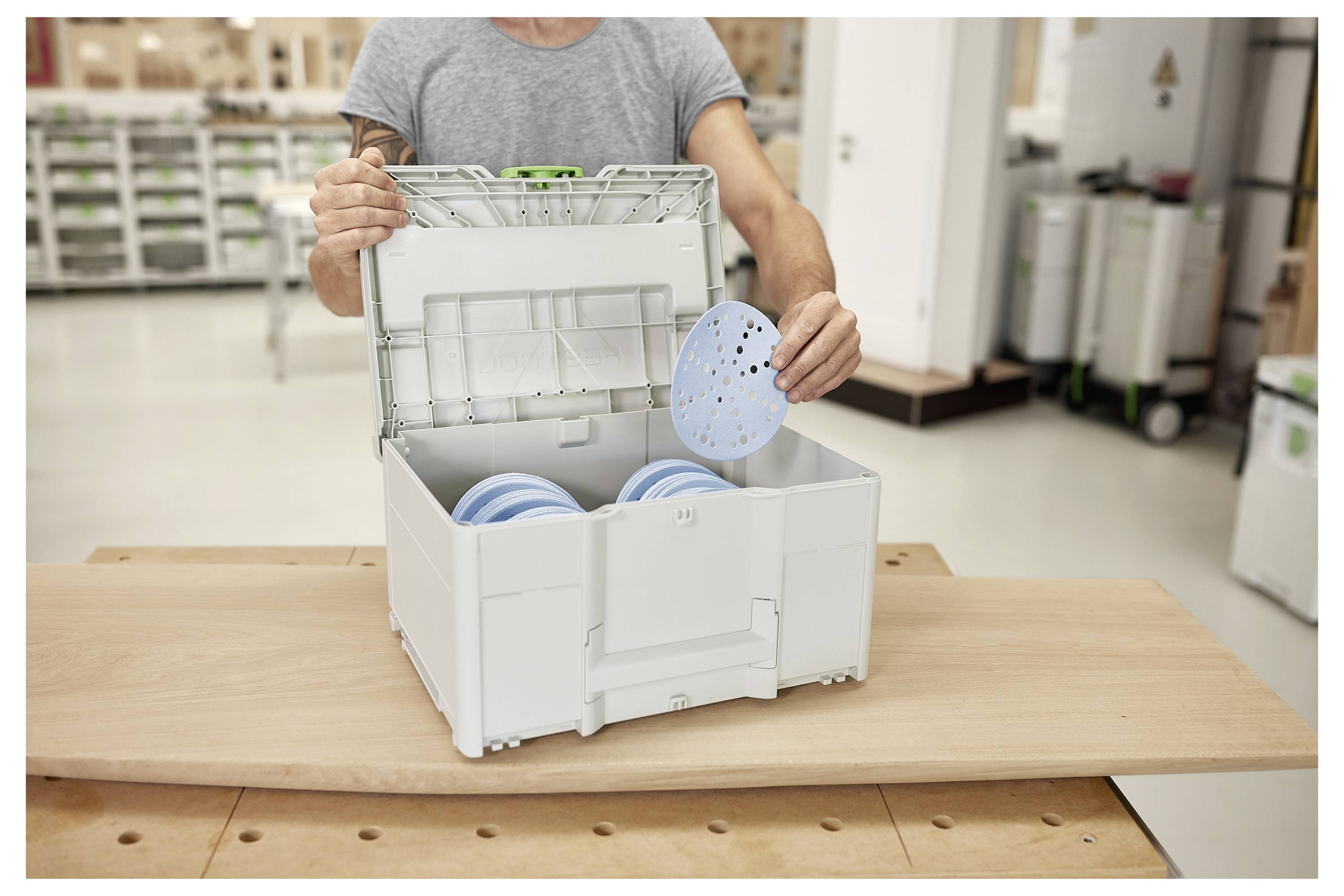 Eine Person, die ein blaues rundes Objekt in eine weiße Lagerkiste mit mehreren Fächern in einer Werkstatt einordnet.