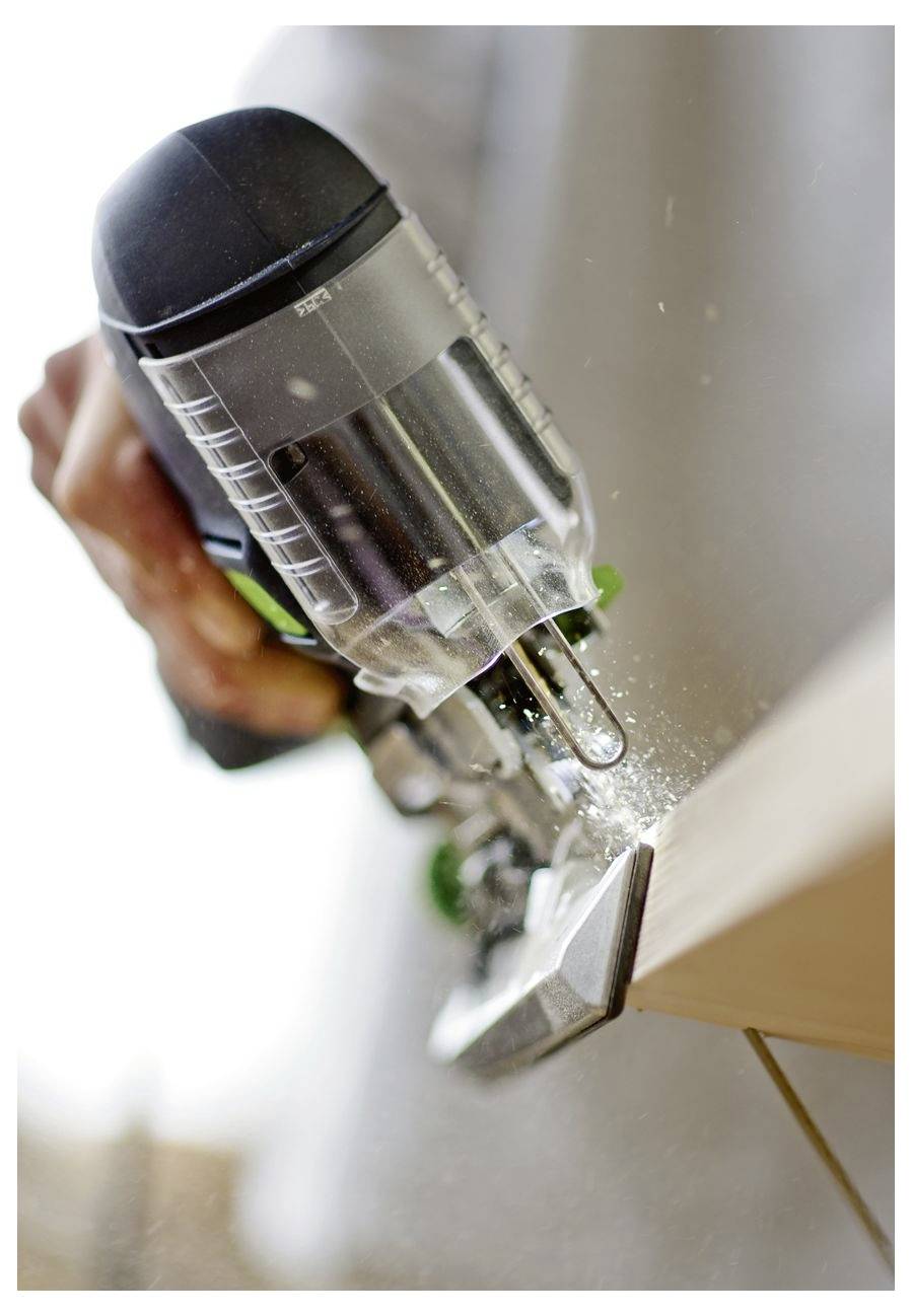 Eine Person bedient eine Stichsäge und schneidet durch ein Holzbrett, wobei Sägemehl entsteht. Das Werkzeug ist angewinkelt und zeigt eine Aktion beim Holzbearbeiten.