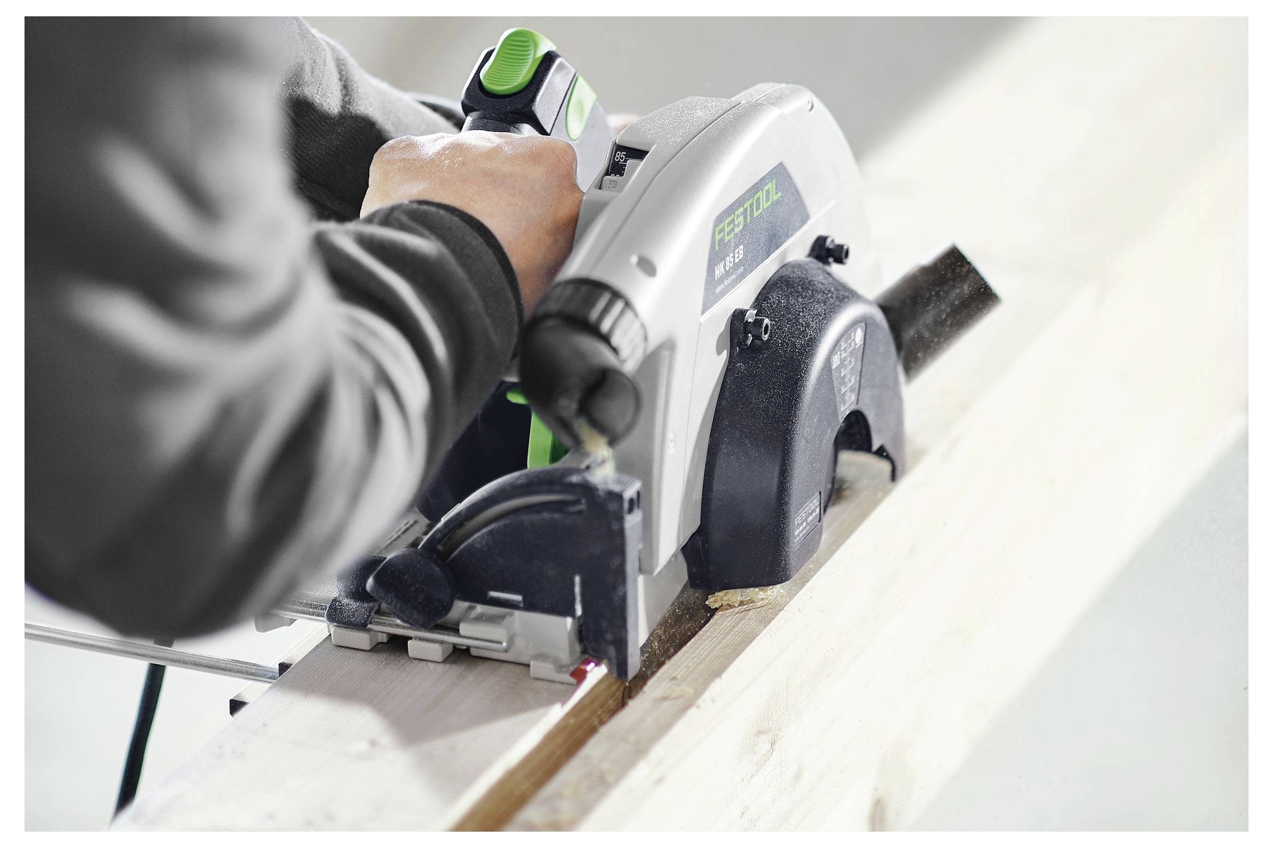 Ein Arbeiter benutzt eine tragbare elektrische Kreissäge, um ein Holzbrett zu schneiden, wobei er sich auf Präzision und Sicherheit in einer Werkstattumgebung konzentriert.